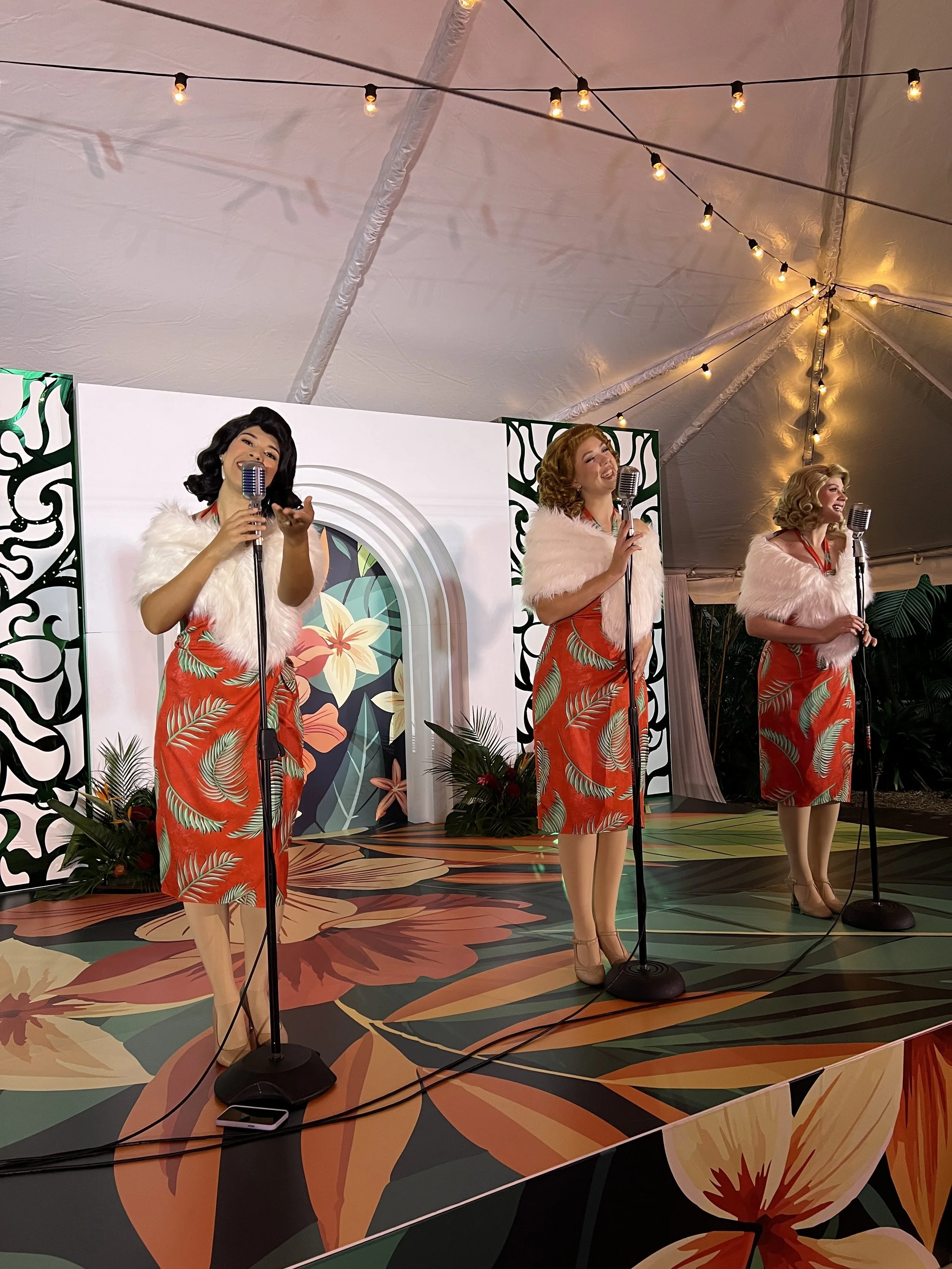 Three performers singing on stage with tropical-themed backdrop at a corporate event in Sarasota