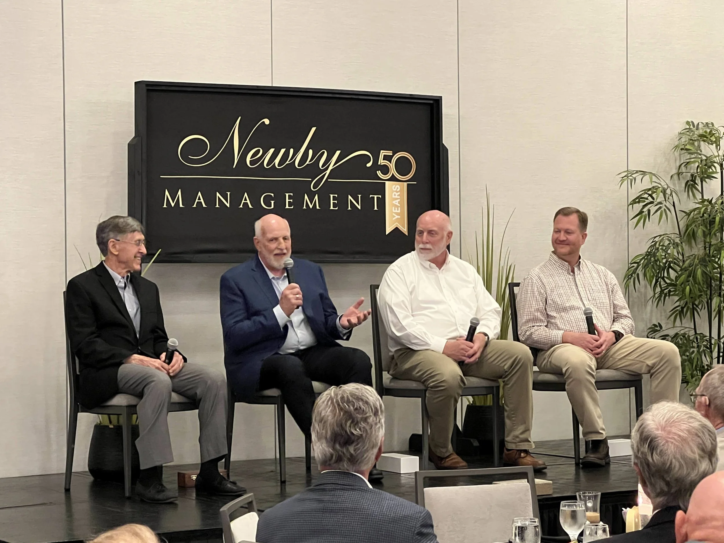 Four-person panel discussion on stage with branded backdrop in Southwest Florida