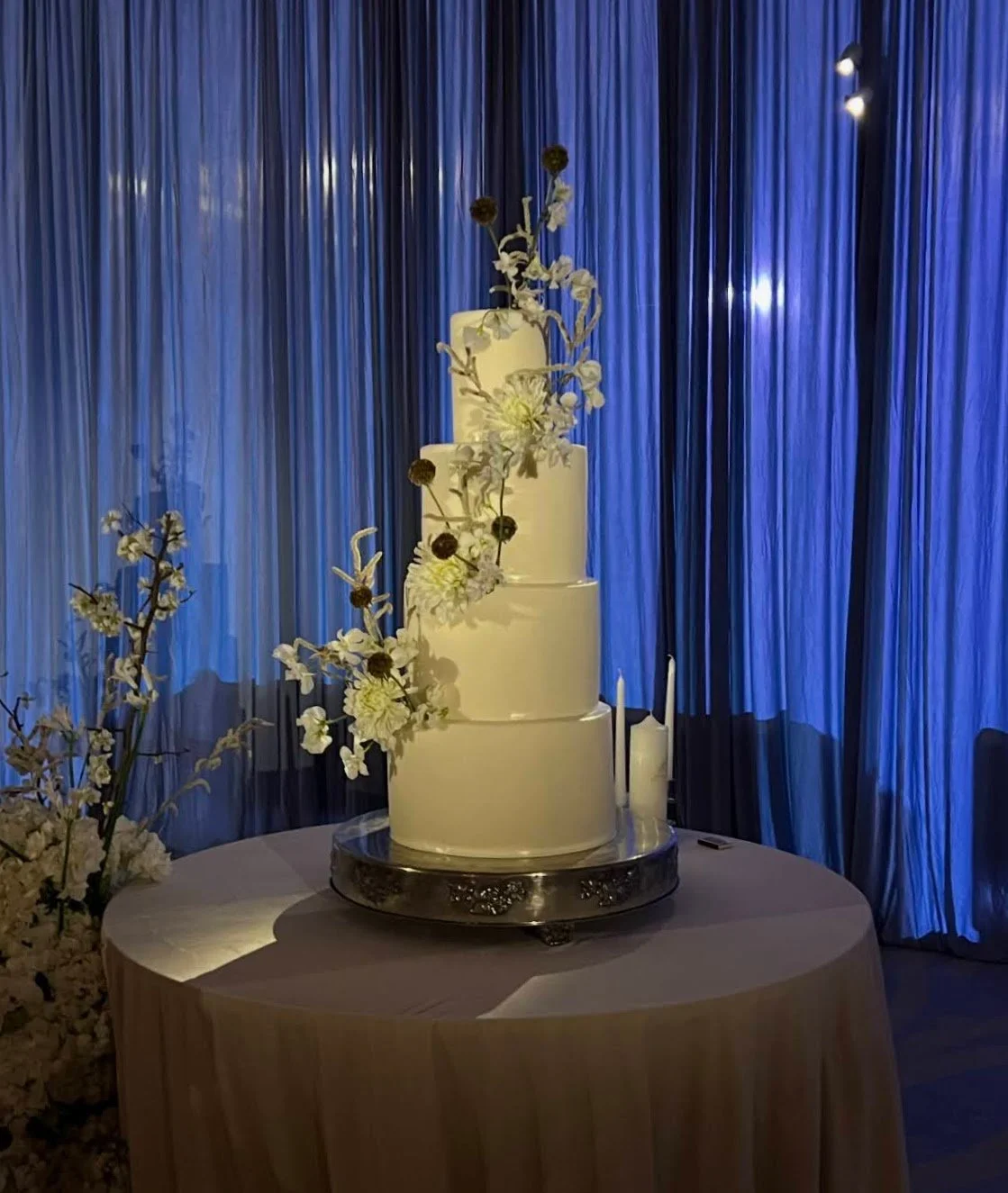 Tiered wedding cake with floral accents against a blue drape in Southwest Florida