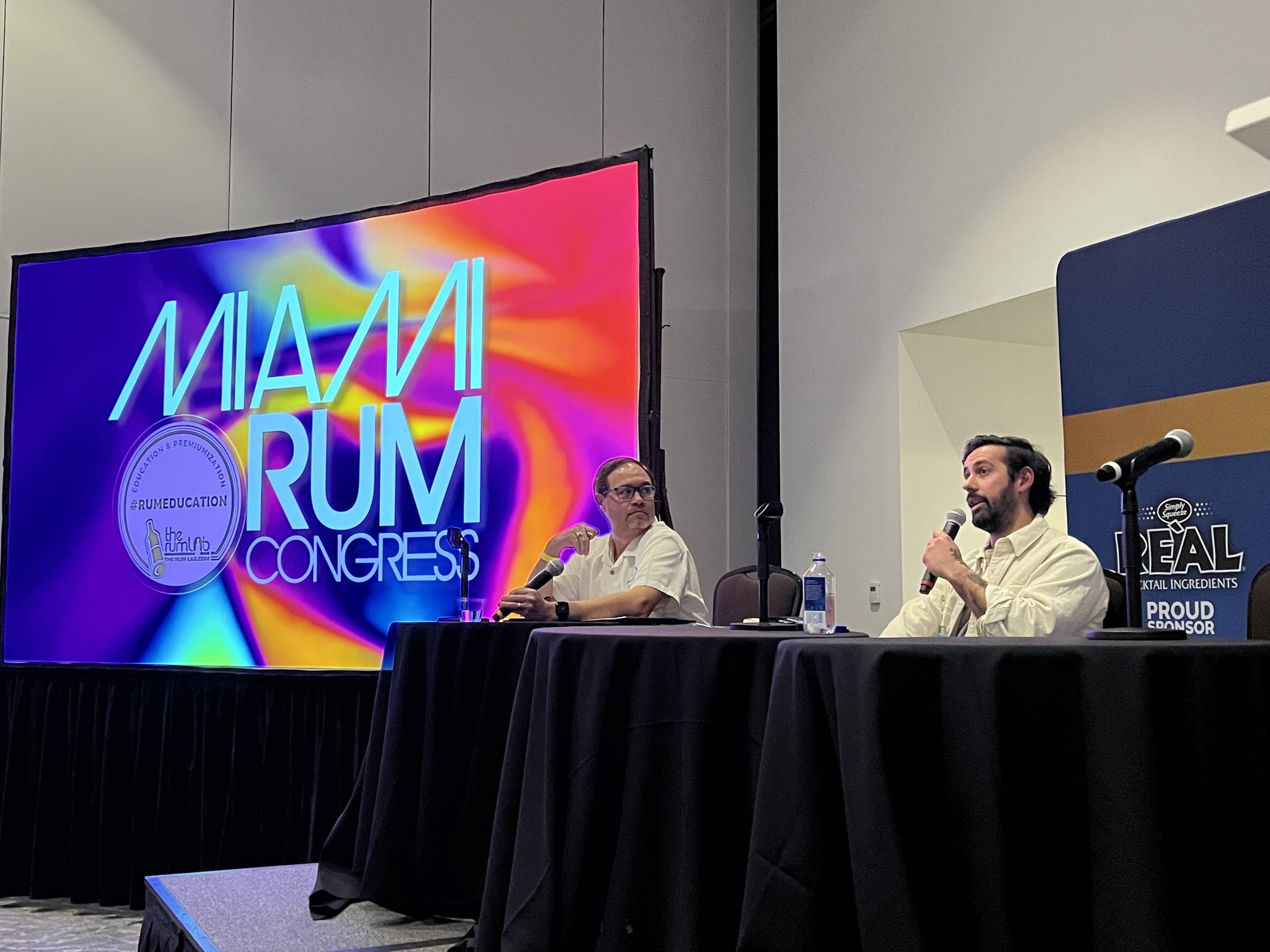 Panel discussion on stage with large branded screen at a conference in Sarasota