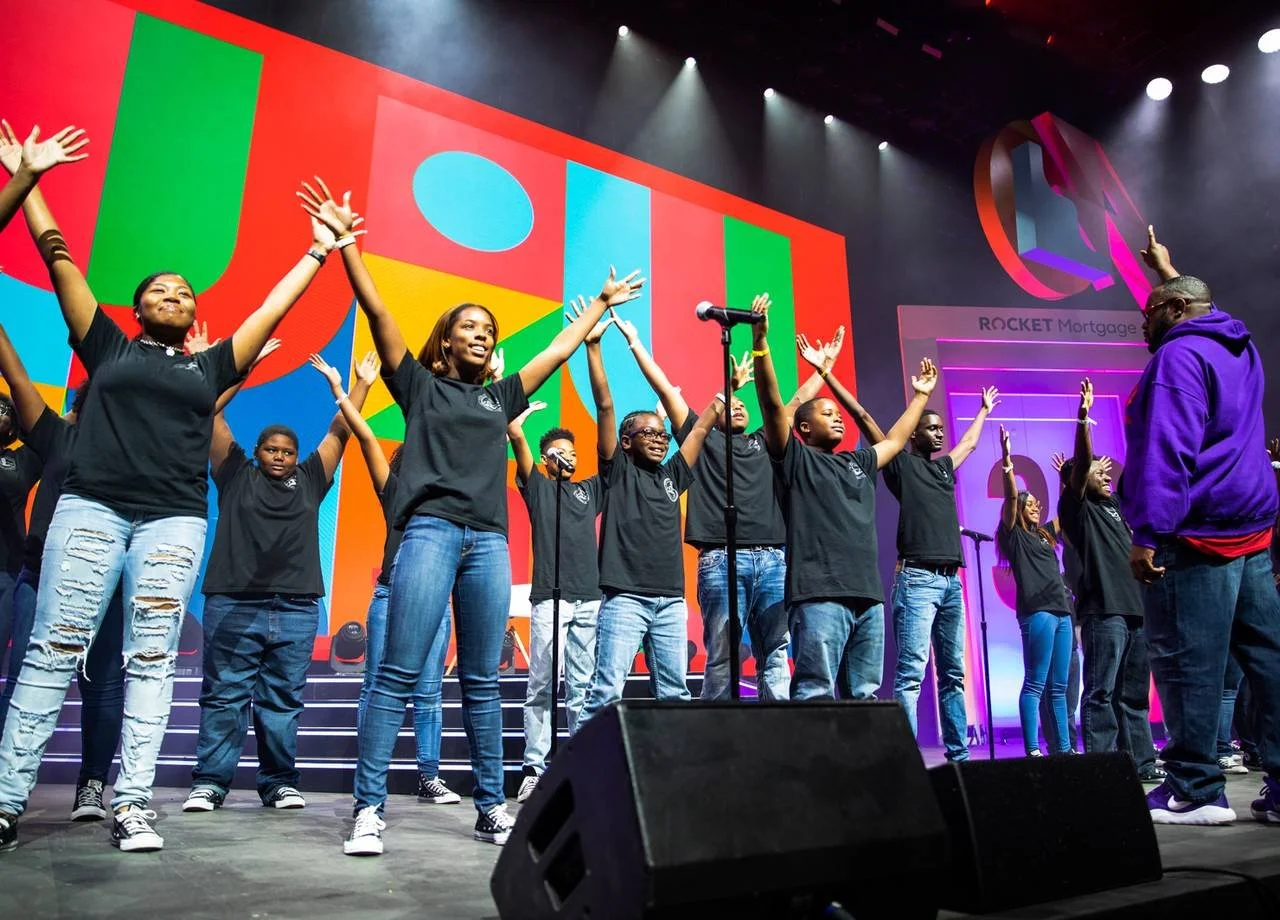 A youth choir performs onstage with arms raised at the Forbes Under 30 Summit