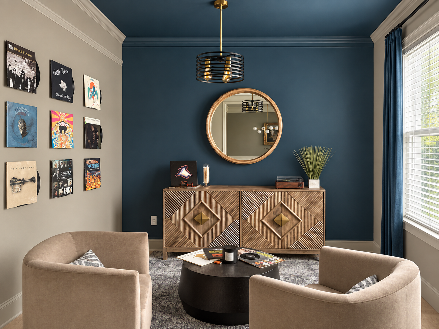 Living room with beige chairs, a black round coffee table, a wooden sideboard with geometric patterns, a round mirror, vinyl records on the wall, and a window with blue curtains.