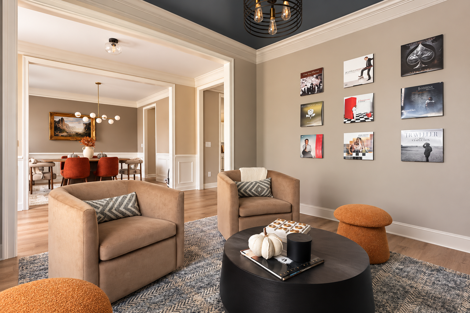 Living room with beige armchairs, a black coffee table, art prints on the wall, and a dining area with a round table and red chairs in the background.
