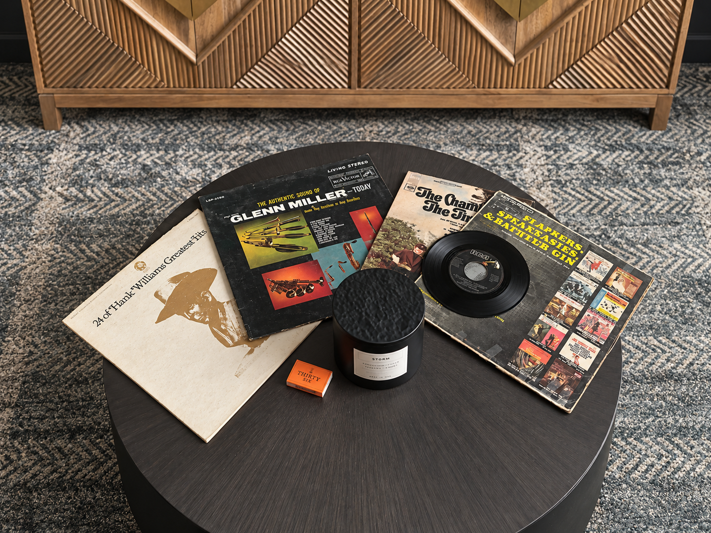 Vintage vinyl records, including albums by Glenn Miller and Hank Williams, a 45 RPM single, and a vinyl record on a black coffee table in a modern living room setting.