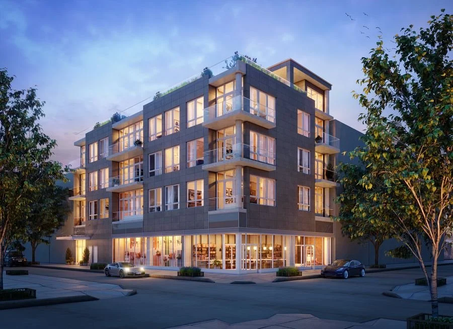 A modern multi-story apartment building with large glass windows and balconies, illuminated at dusk, with trees and parked cars in front.