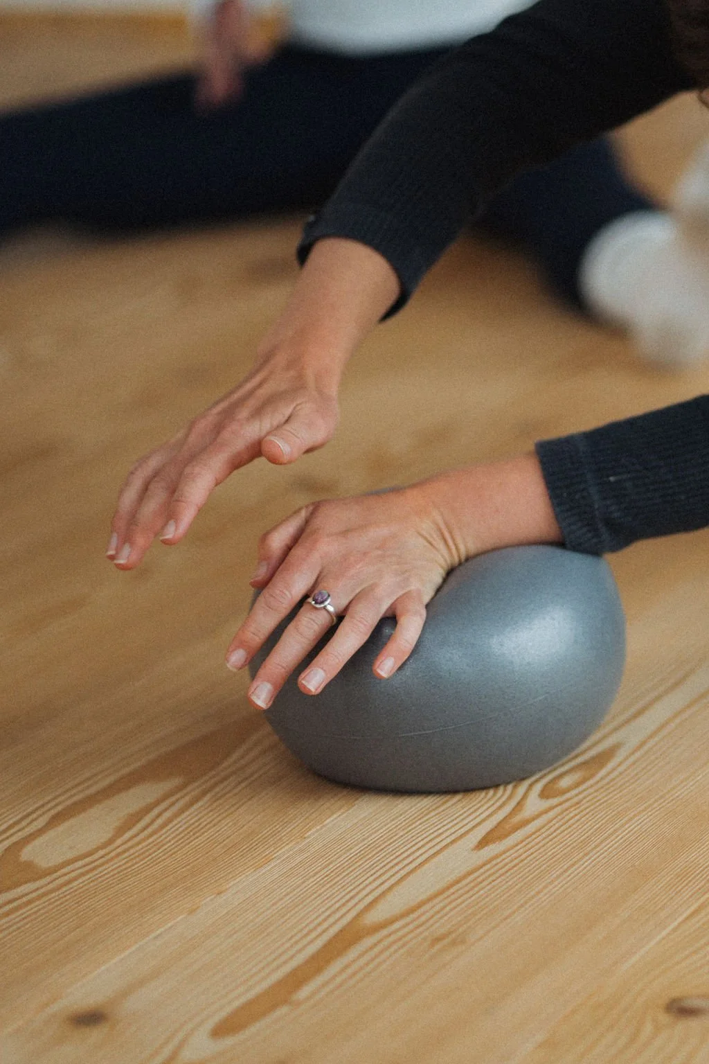 Person macht Yoga auf einer Holzboden, mit einem grauen Ball als Unterstützung.