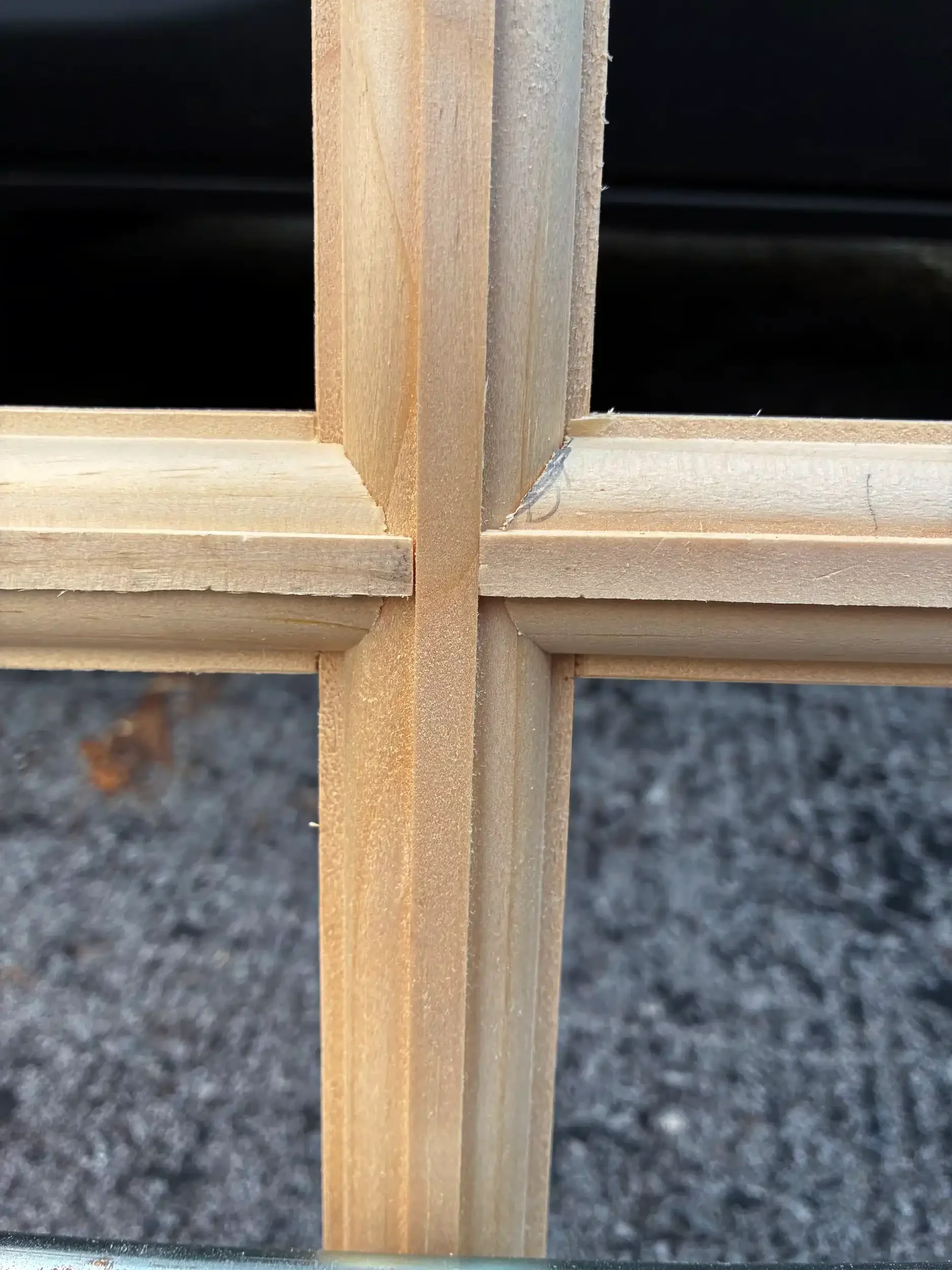 Close-up of a corner joint of a wooden frame or structure, with two vertical and two horizontal pieces of wood joined together.