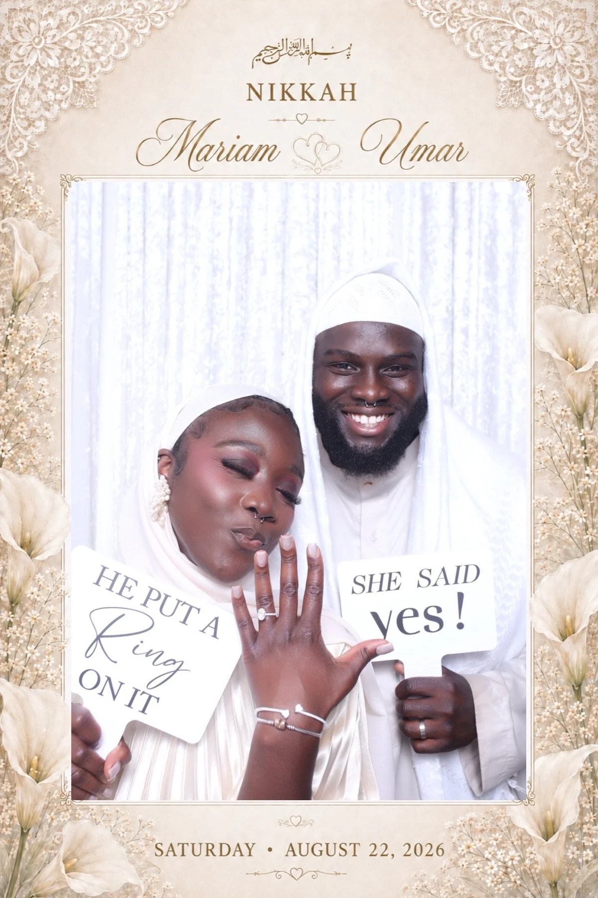 A wedding photo with a couple wearing white traditional attire, holding signs that say "HE PUT A RING ON IT" and "SHE SAID YES!" The woman is showing her engagement ring and the man is smiling at the camera. The background is a white curtain, and the border of the photo has floral decorations. The date at the bottom reads Saturday, August 22, 2026.