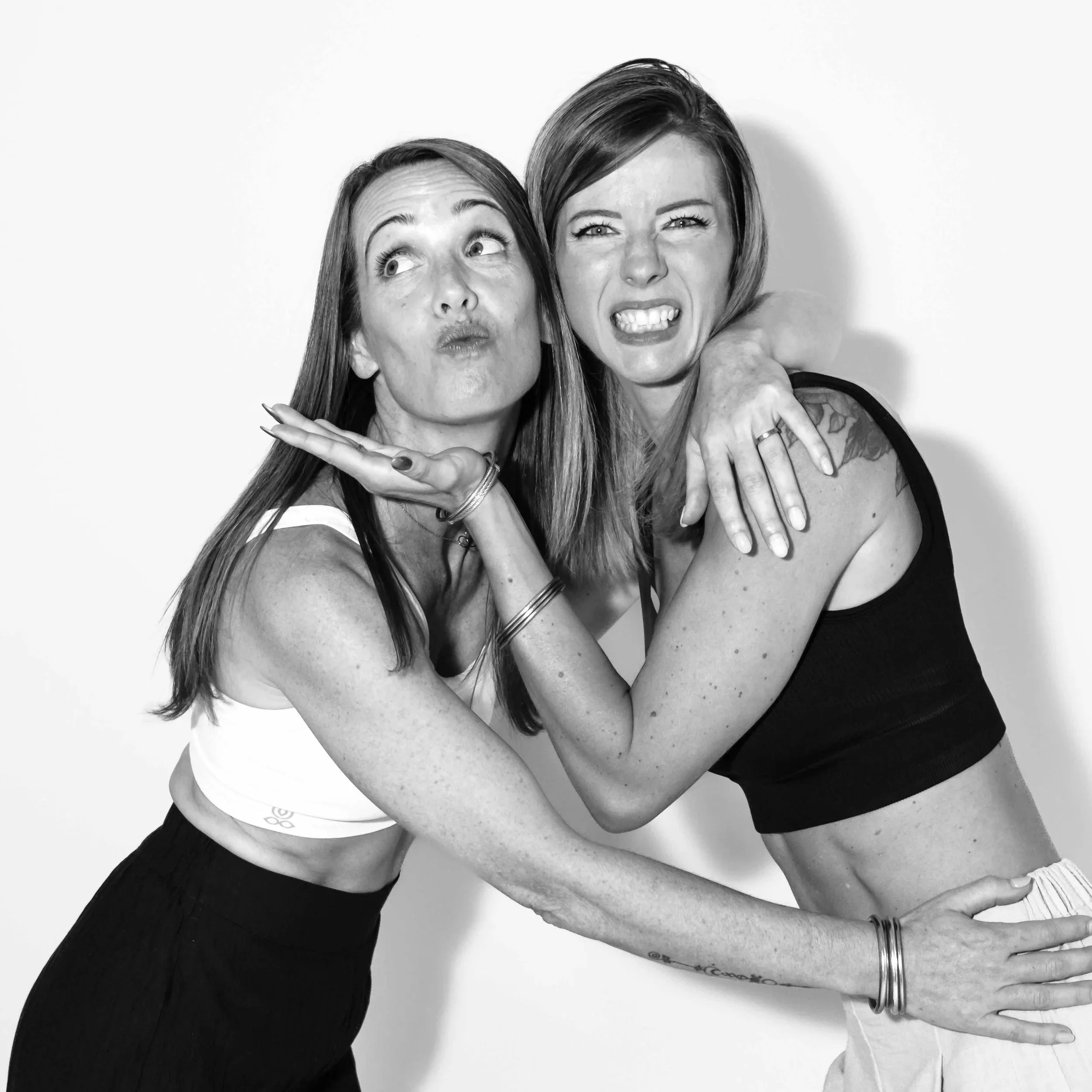 Deux femmes posant de manière expressive, une avec un regard vers le haut et une expression étonnée, l'autre montrant les dents dans une grimace, toutes deux en vêtements décontractés, contre un fond blanc.