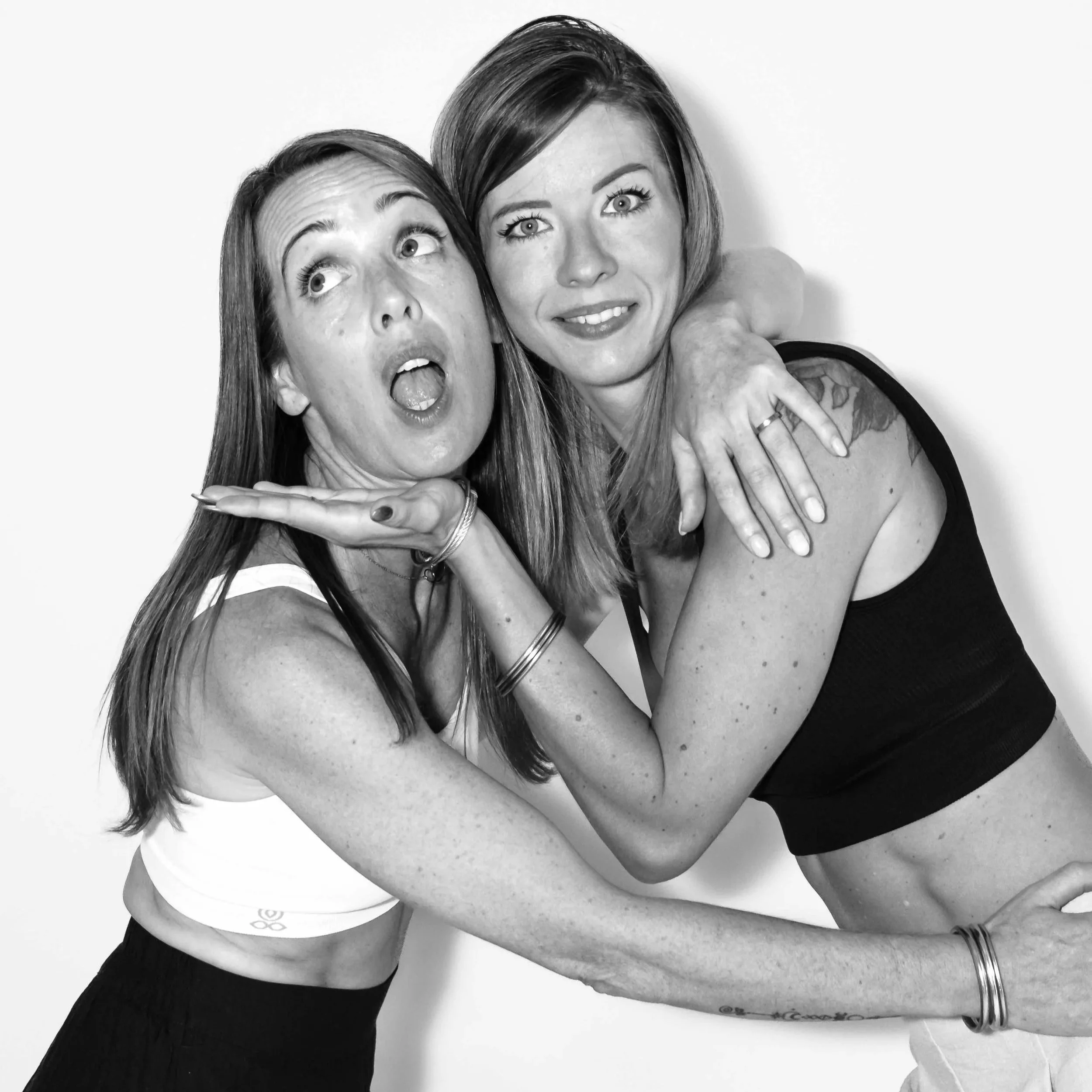 Deux femmes dans une pose amicale, l'une derrière l'autre, avec des expressions joyeuses. La femme en avant porte un T-shirt blanc, et celle derrière un haut noir. L'image est en noir et blanc.