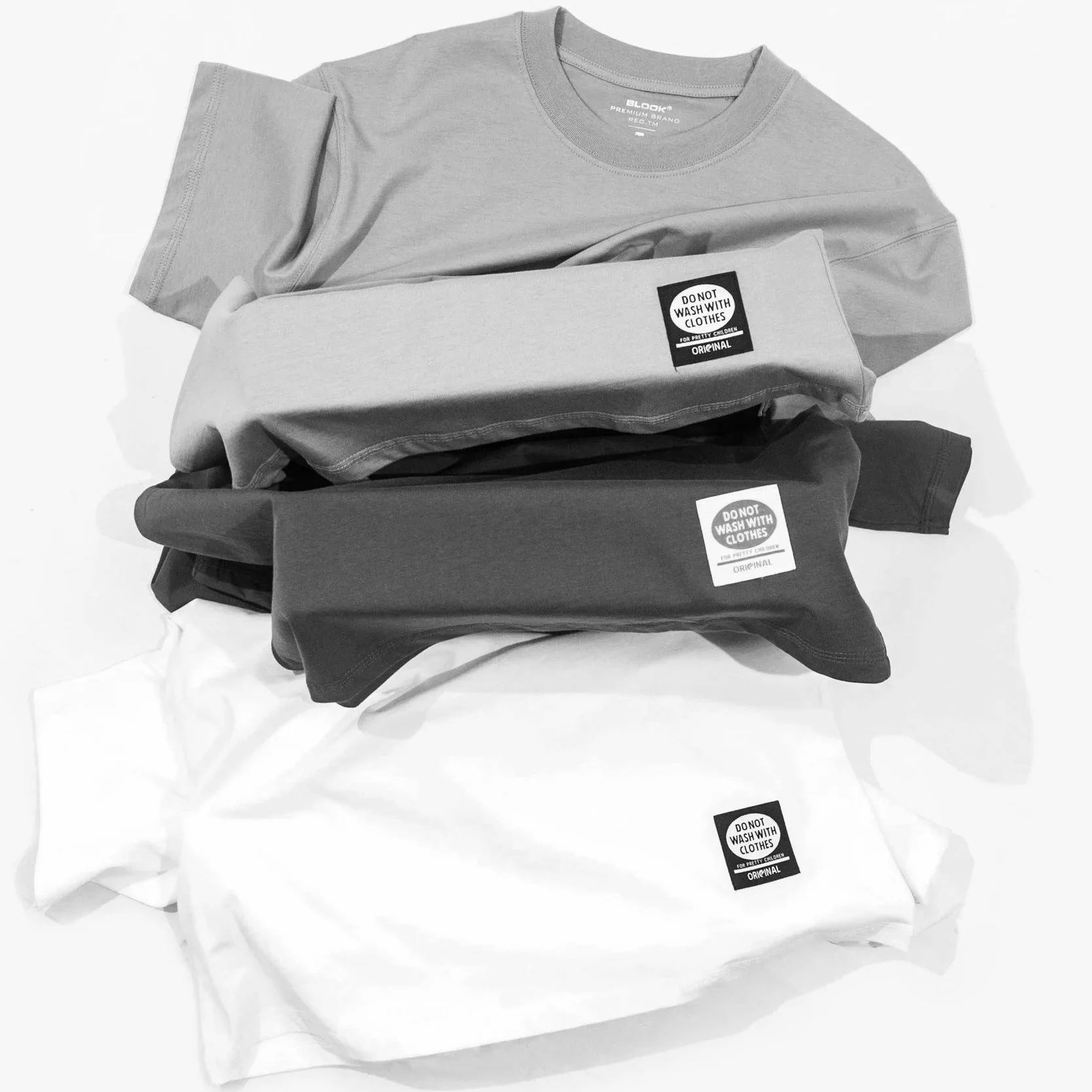 T-shirts pliés dans différentes couleurs avec étiquettes, certains portent une étiquette indiquant « Ne pas laver avec d'autres vêtements ».