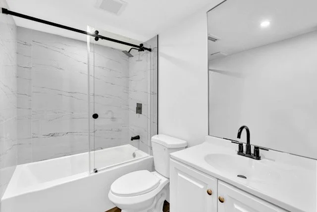 Modern bathroom with a bathtub, glass shower enclosure, toilet, and white vanity with a black faucet.