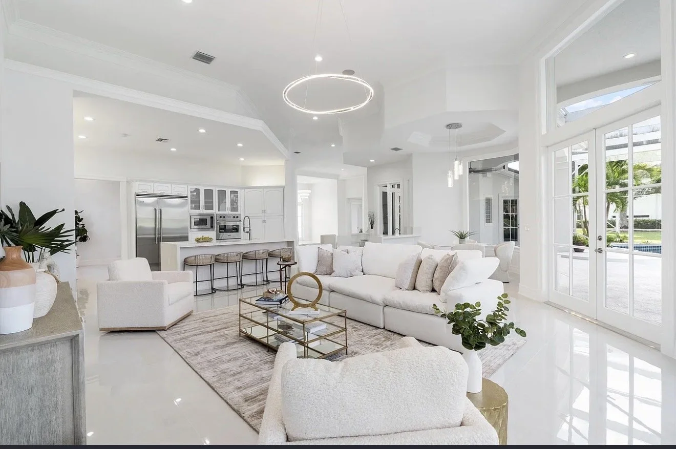 Bright, modern living room with white furniture, large windows, and a view of a pool outside.