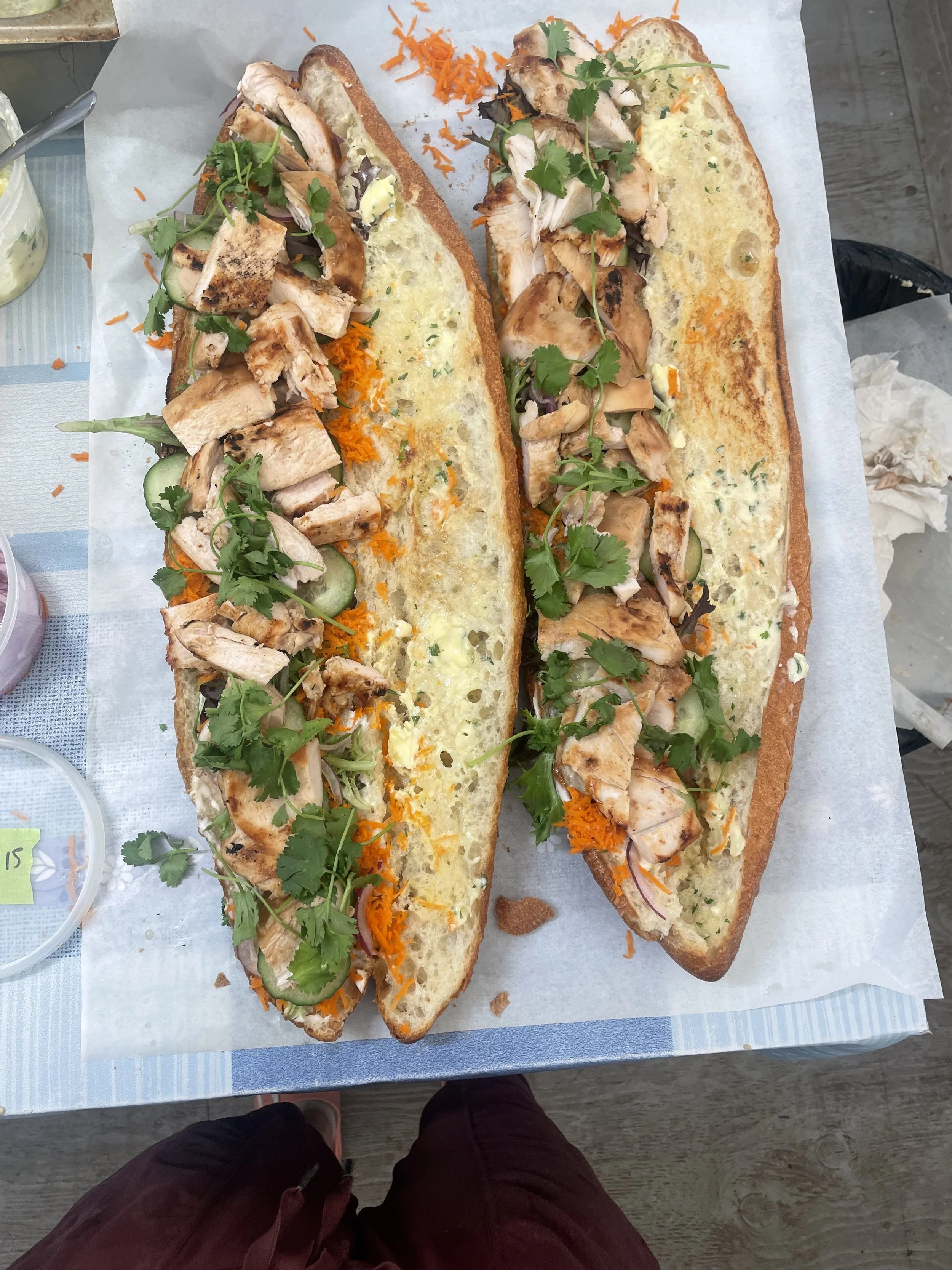 Two long toasted bread slices topped with grilled chicken, fresh cilantro, cucumber slices, shredded carrots, and a layer of melted cheese prepared by a Revelstoke private chef.