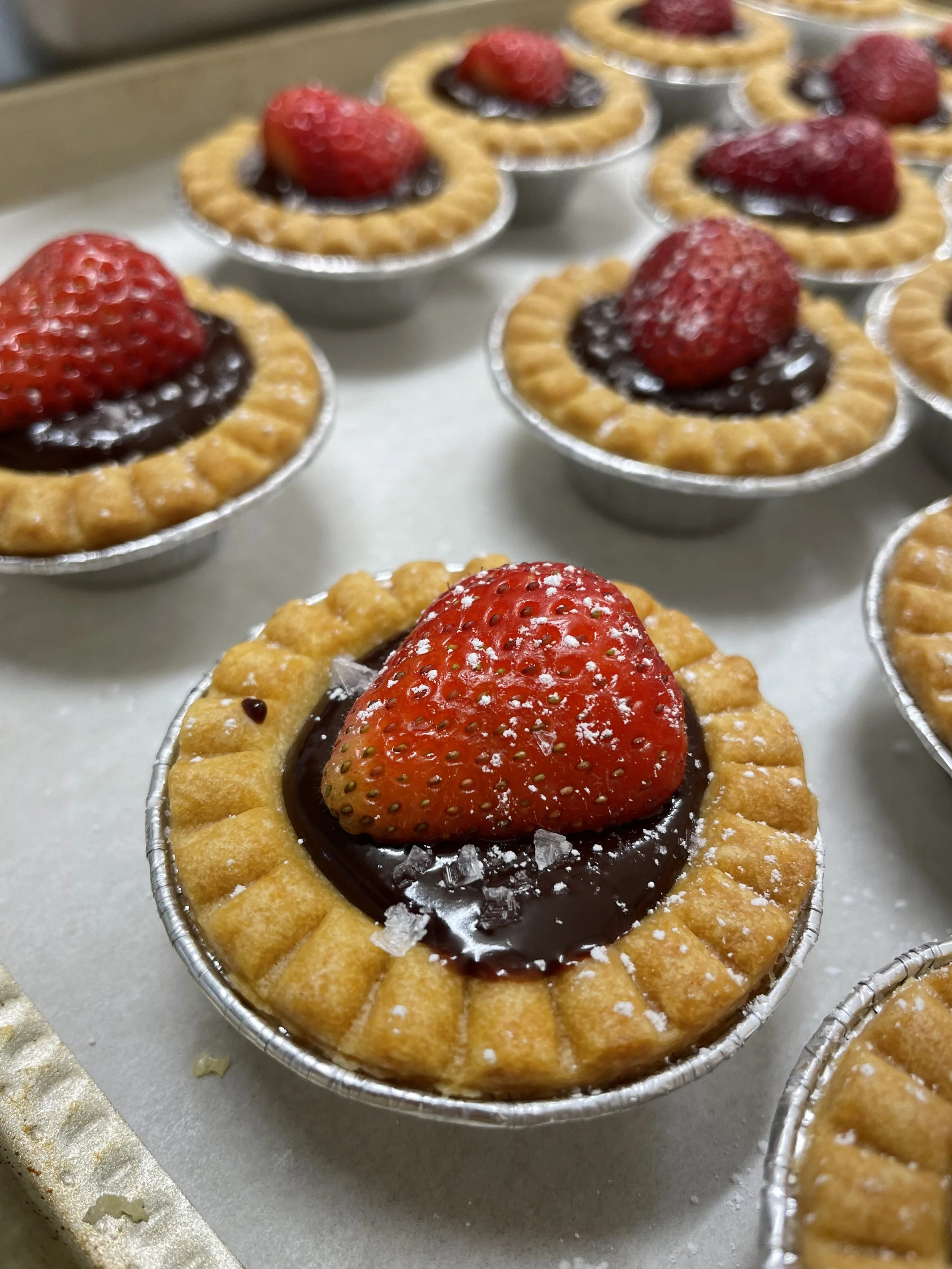 Mini strawberry tartlets with a shortbread crust, filled with chocolate ganache, topped with fresh strawberries and a sprinkle of sea salt prepared by a Revelstoke private chef.