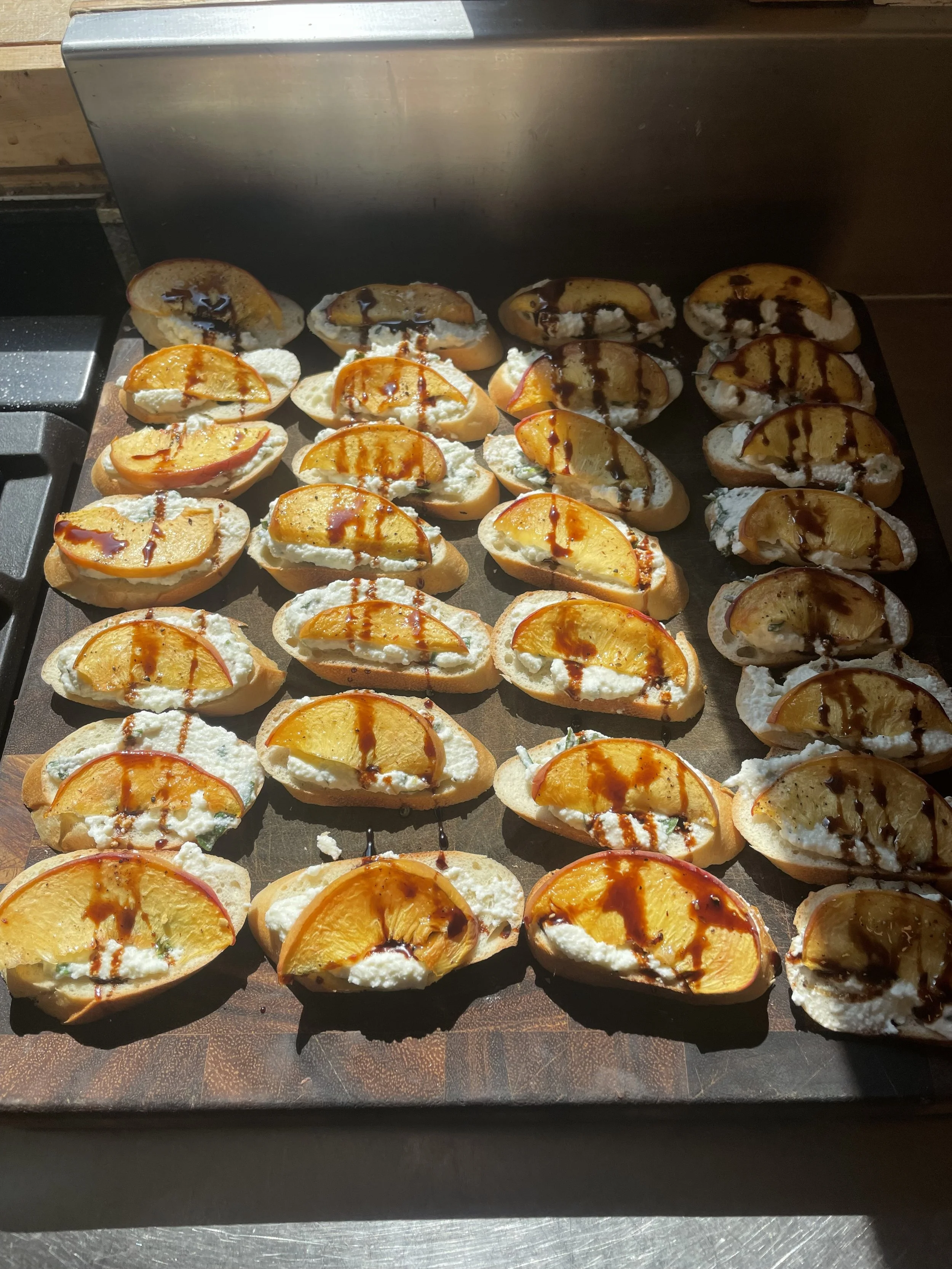 Several slices of bread topped with cream cheese, peach slices, and drizzled with balsamic reduction on a baking sheet by a private chef in Revelstoke.