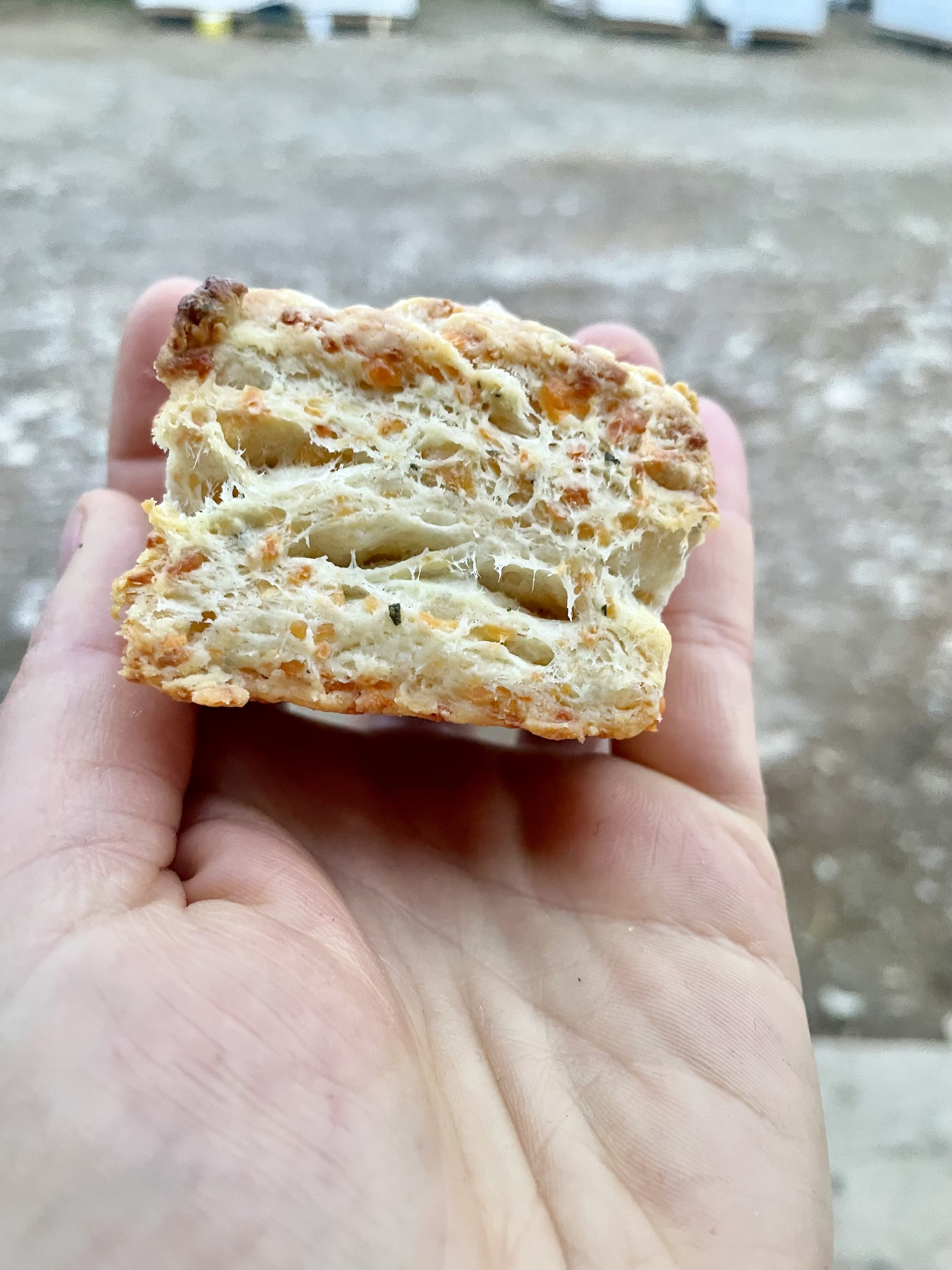 Close-up of a person's hand holding a slice of pepperoni pizza with melted cheese, with an outdoor area in the background prepared by a Revelstoke private chef.