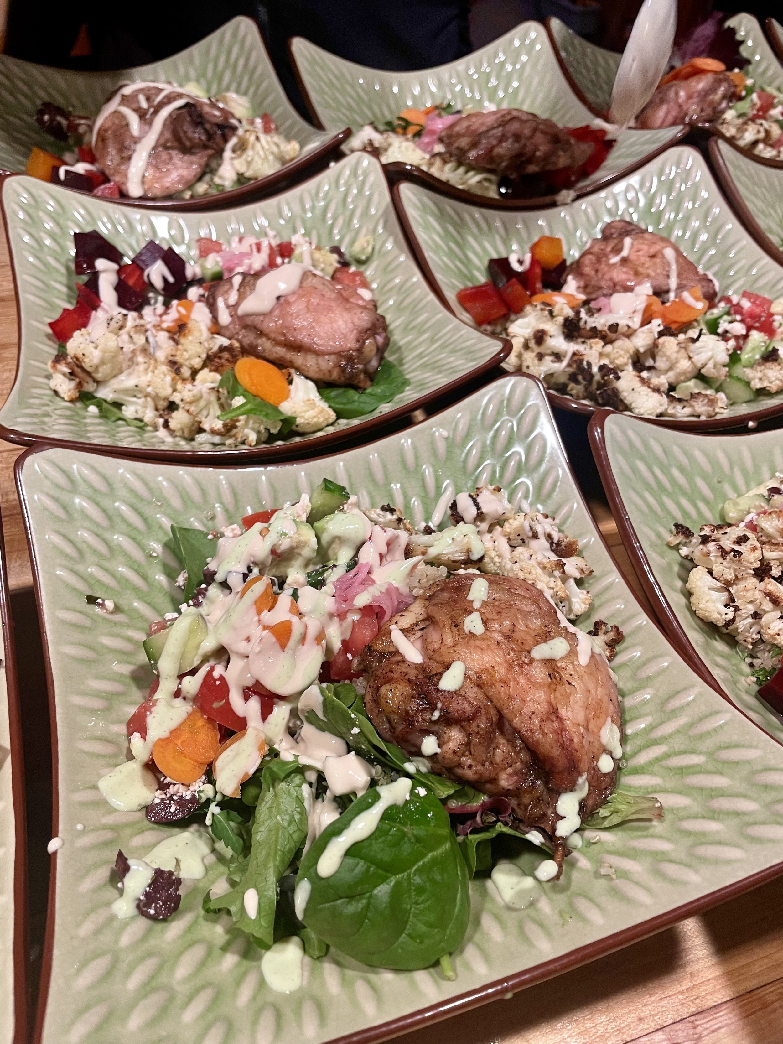 Multiple ceramic plates with salads, cooked meats, and vegetables on a wooden table prepared by a Revelstoke private chef.