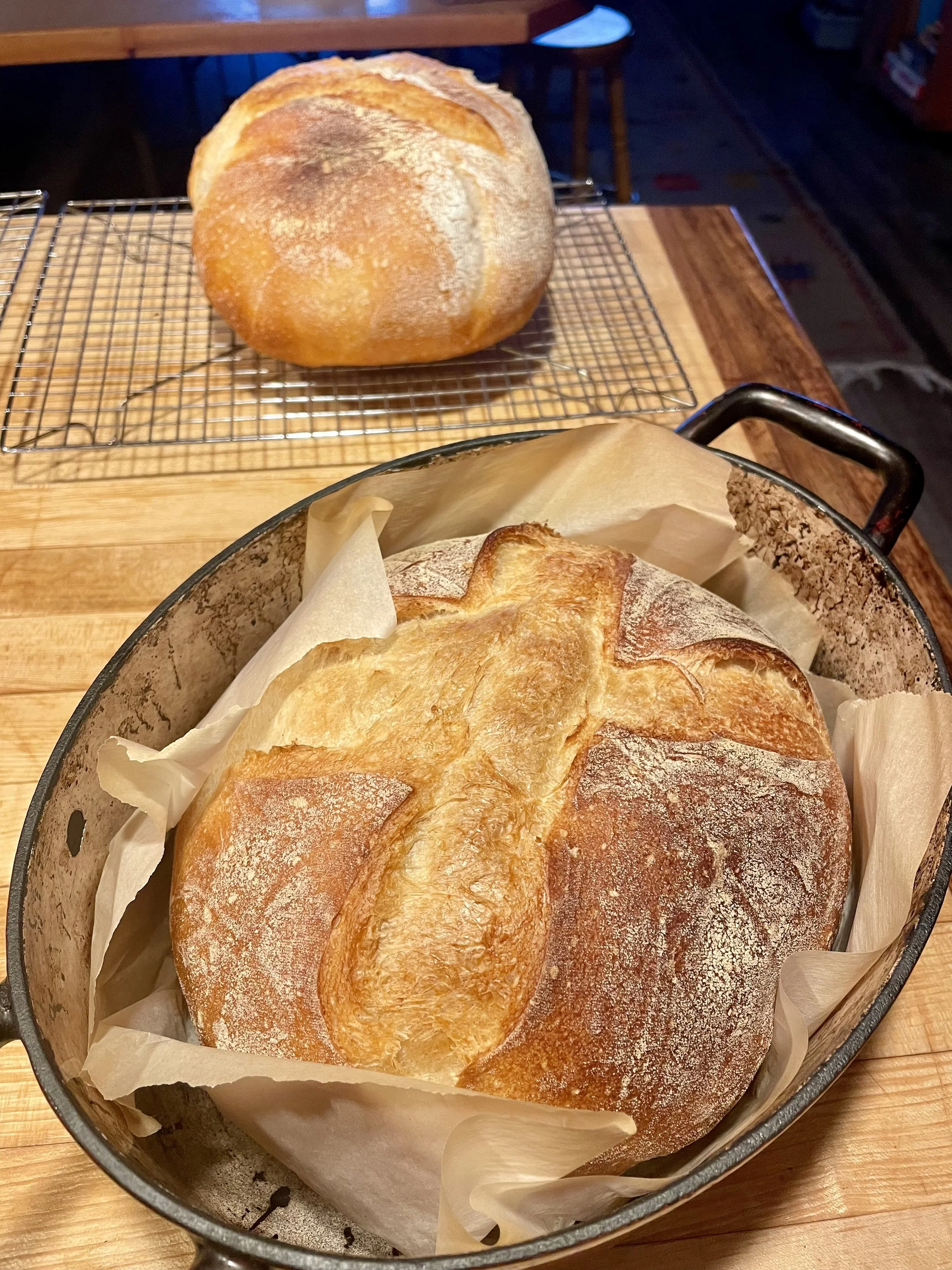 A loaf of freshly baked bread in a baking pan, with another loaf cooling on a wire rack on a wooden table prepared by a Revelstoke private chef.