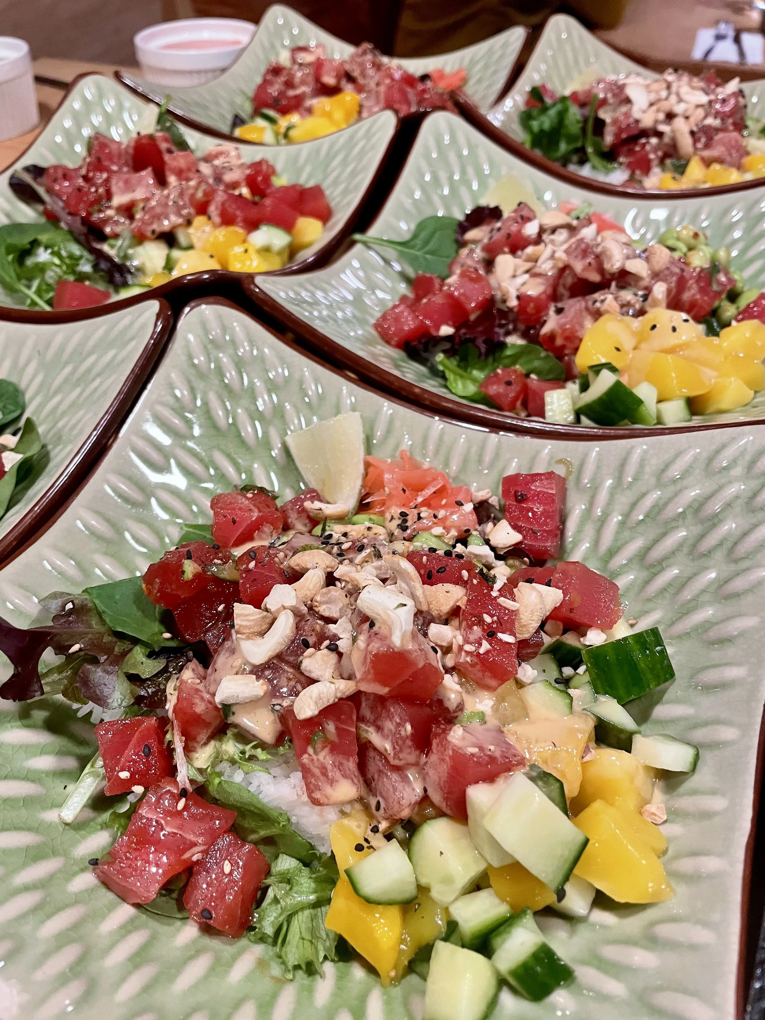 A close-up of four ceramic bowls filled with diced raw vegetables and chopped tuna, garnished with seeds and herbs, placed on a table prepared by a Revelstoke private chef.