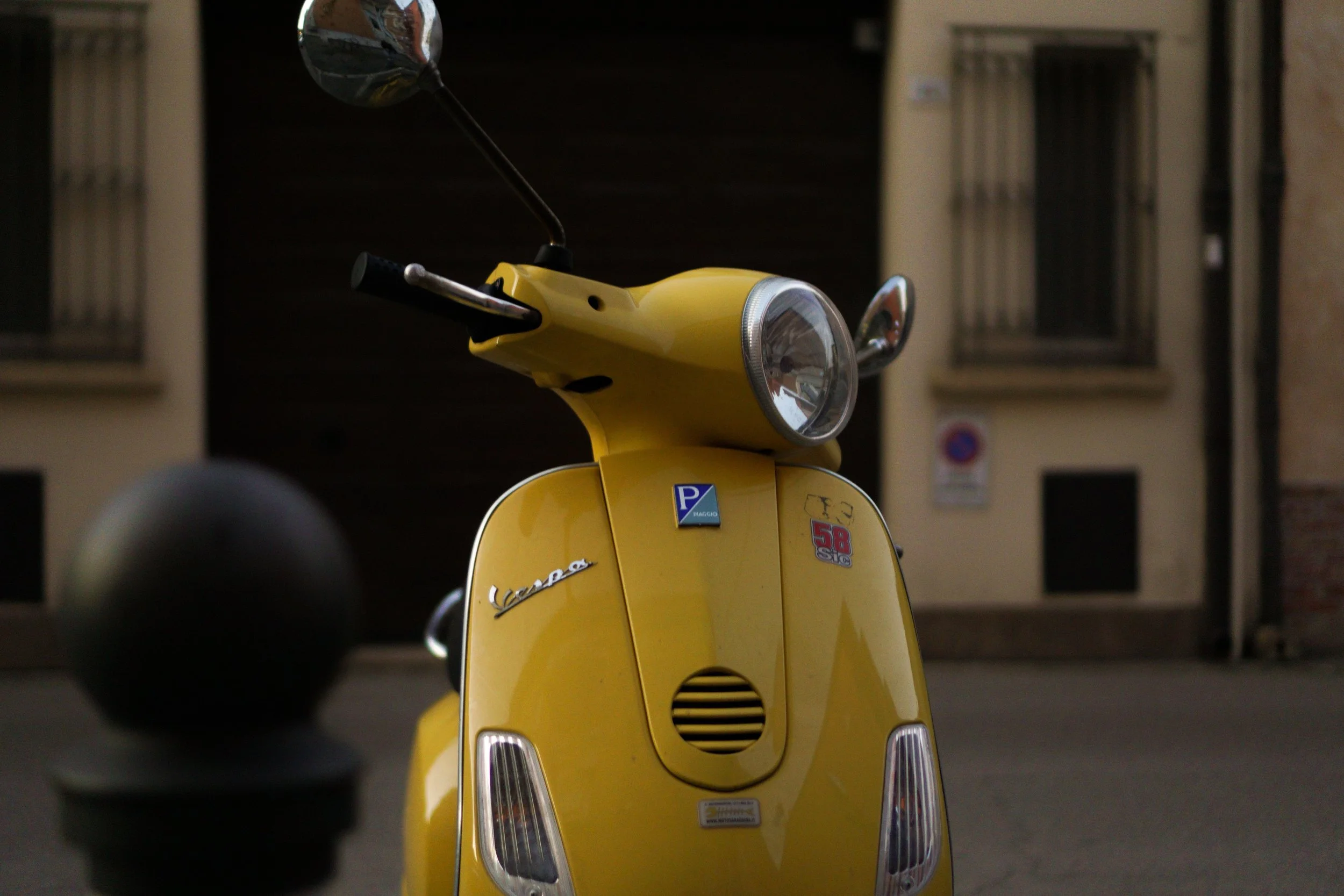 Yellow Vespa scooter parked on a city street at night, with building windows in the background.