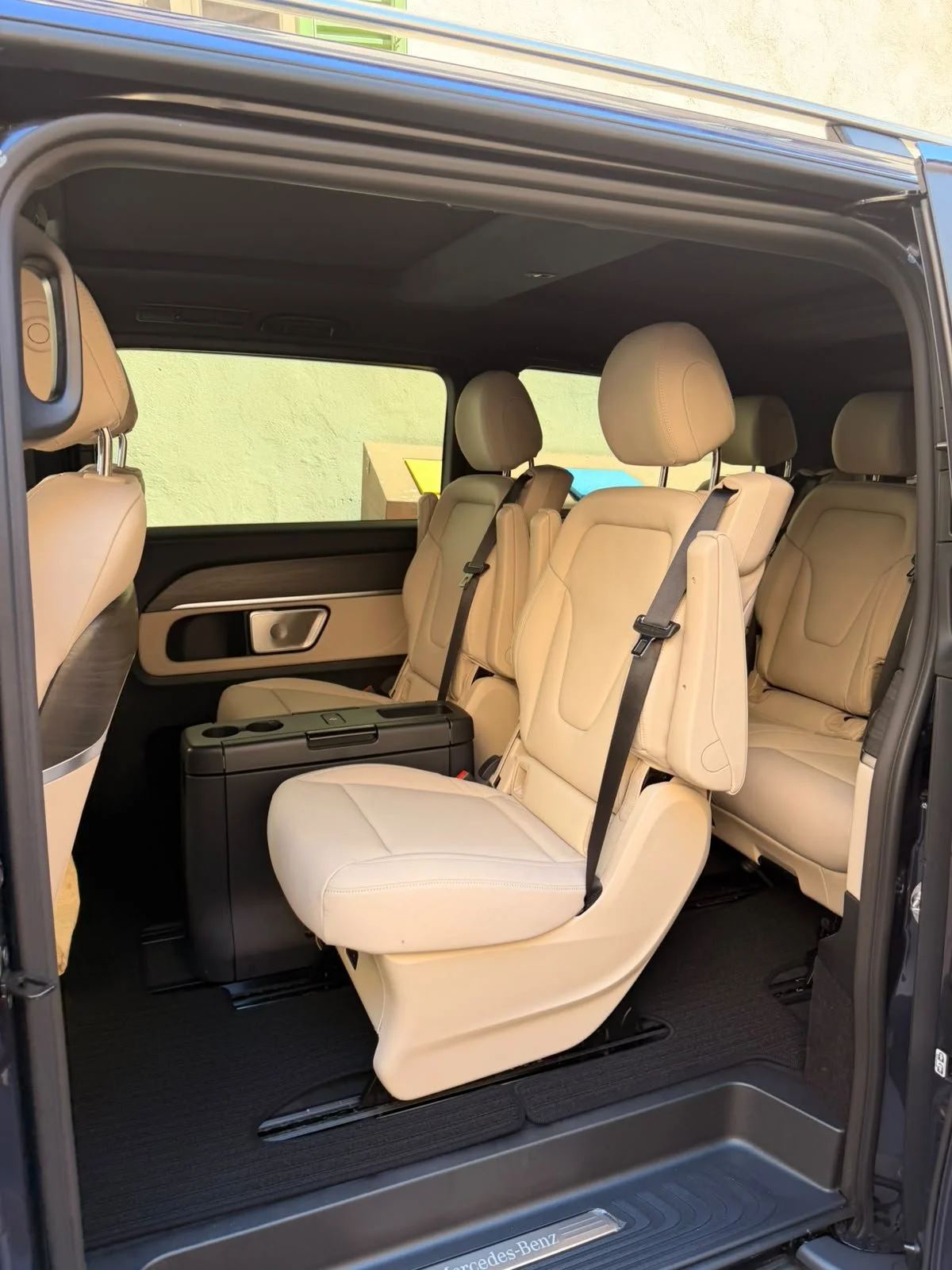 Interior of a luxury van with beige leather seats, some upright and some folded down, and black seat belts.
