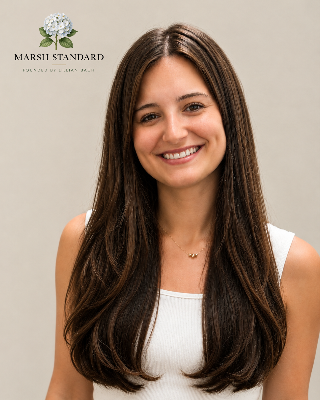 A young woman with long dark hair smiling at the camera, wearing a white sleeveless top and a delicate necklace, standing against a plain background. In the top left corner, there is a logo with a white hydrangea flower and the text 'Marsh Standard Founded by Lillian Bach.'