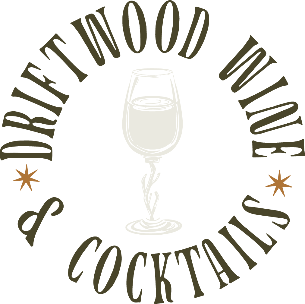 A logo with a wine glass in the center, featuring a swirling stem and a filled bowl. The text "DRINK EAT IN FOOD IN on" curves around the top and bottom, with two small decorative stars flanking the sides.