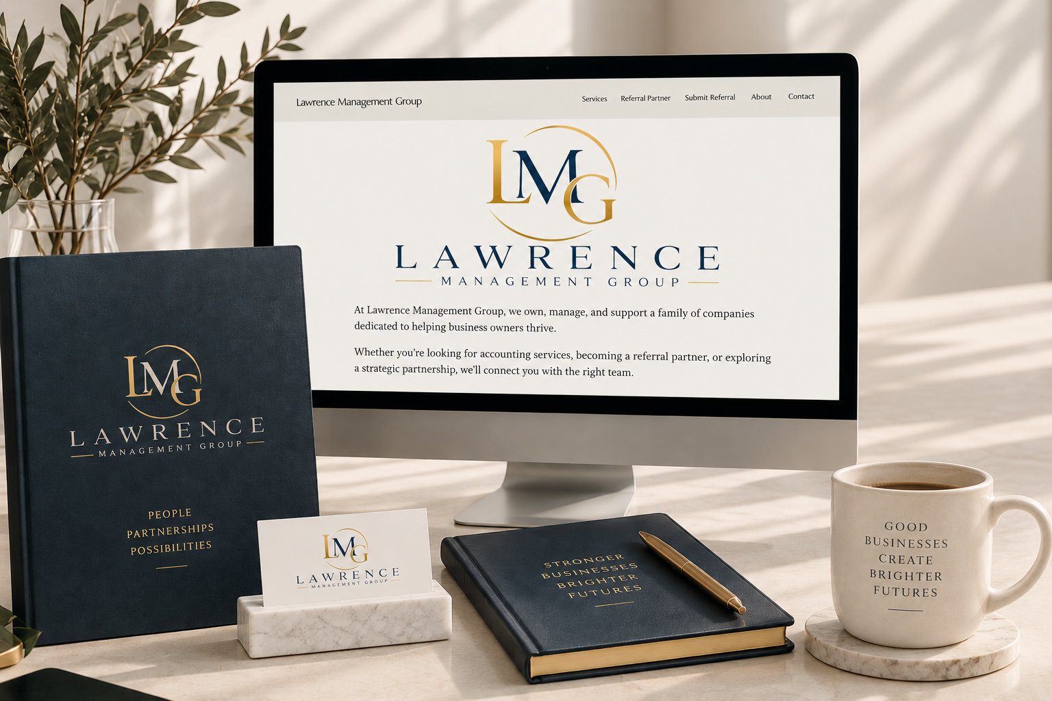 Desk setup with Lawrence Management Group branded materials, a computer monitor displaying the company's website, a coffee mug with an inspirational message, a notebook with gold lettering, a business card holder, and a small plant in the background.
