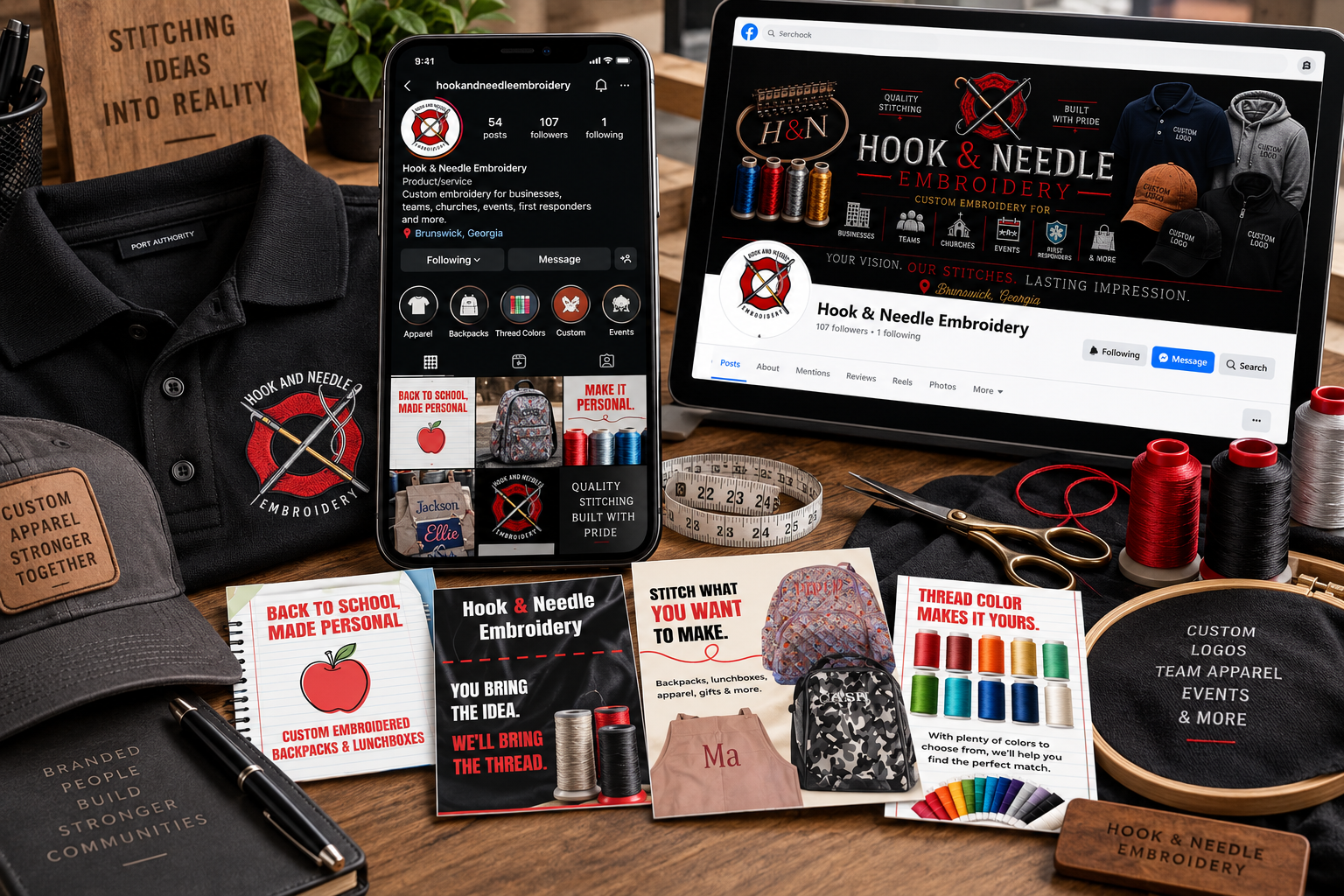 A tabletop display of embroidery and customization items including embroidered apparel, a phone showing a social media profile for 'hookandneedleeembroidery,' a laptop with a Facebook page for 'Hook & Needle Embroidery,' spools of thread in various colors, scissors, a measuring tape, embroidery patches, brochures, a cap, and other accessories related to embroidery and custom apparel.