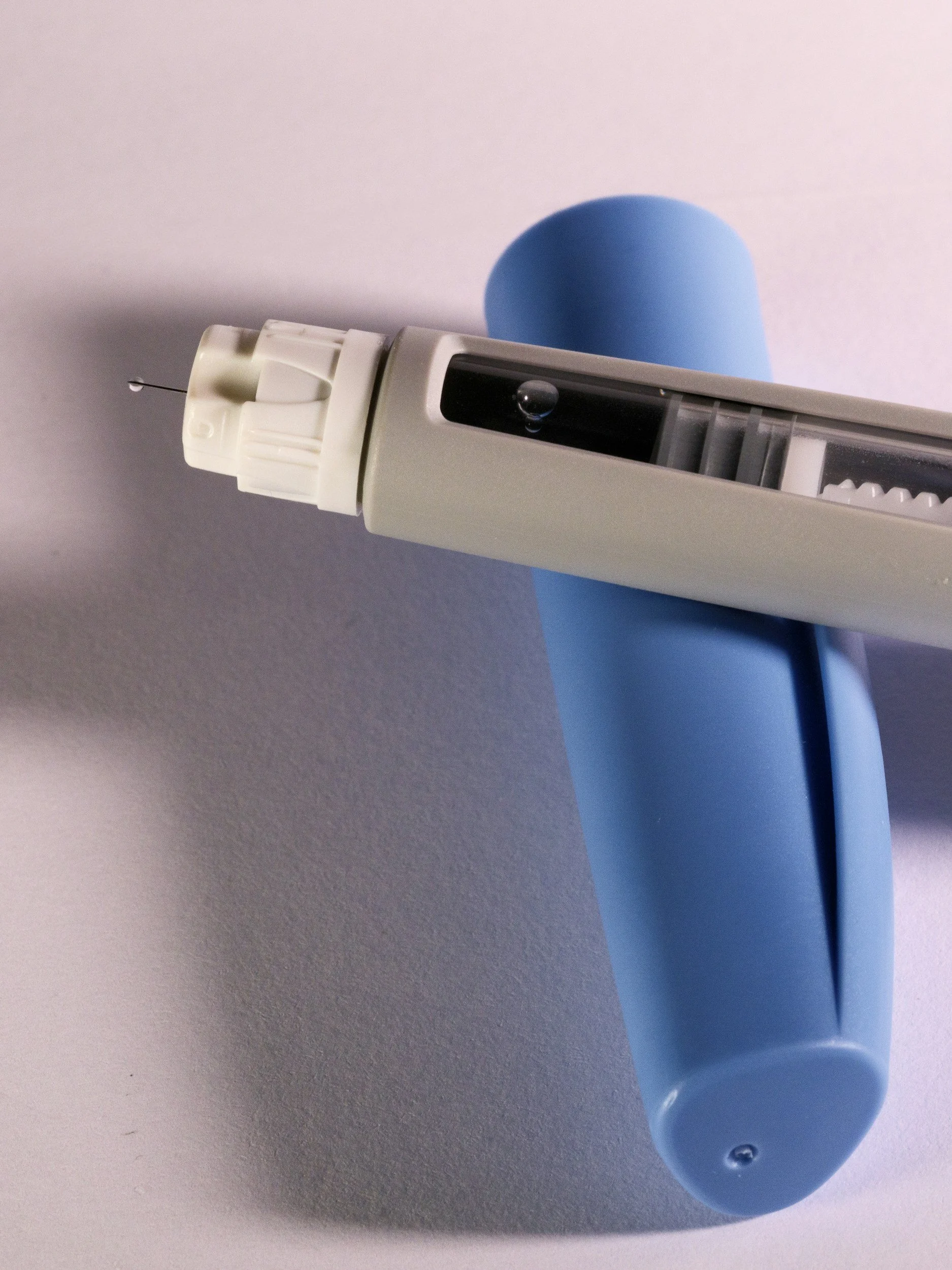 A blue and white insulin pen with a needle attached, resting on a white surface.