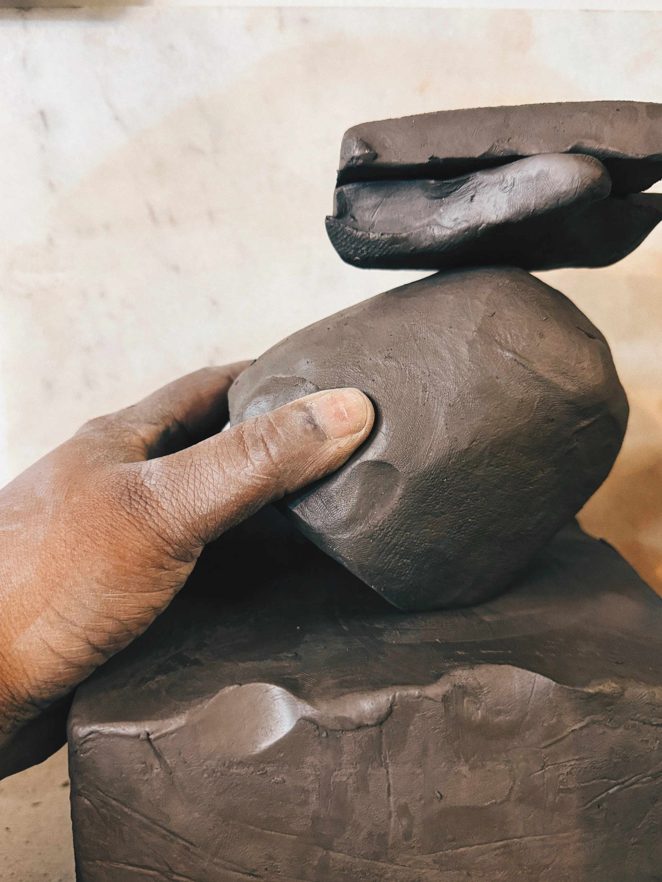 Close-up of a person's hand pressing a piece of gray clay or mud sculpture.