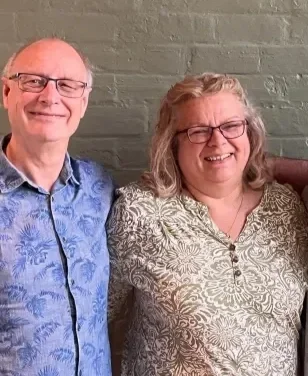 Four smiling people standing together in front of a gray brick wall.