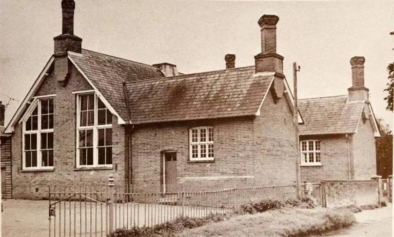 An old black-and-white photo of a brick house with large windows, a sloped roof, and tall chimneys.