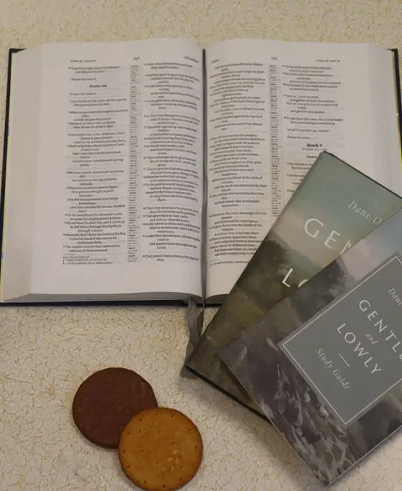 An open Bible, two copies of a book titled 'Gentle and Lowly' by Dane Ortlund, and two cookies on a light-colored surface.