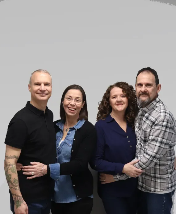 Four adults standing together against a gray background, smiling, with two women in the middle and two men on the outside.