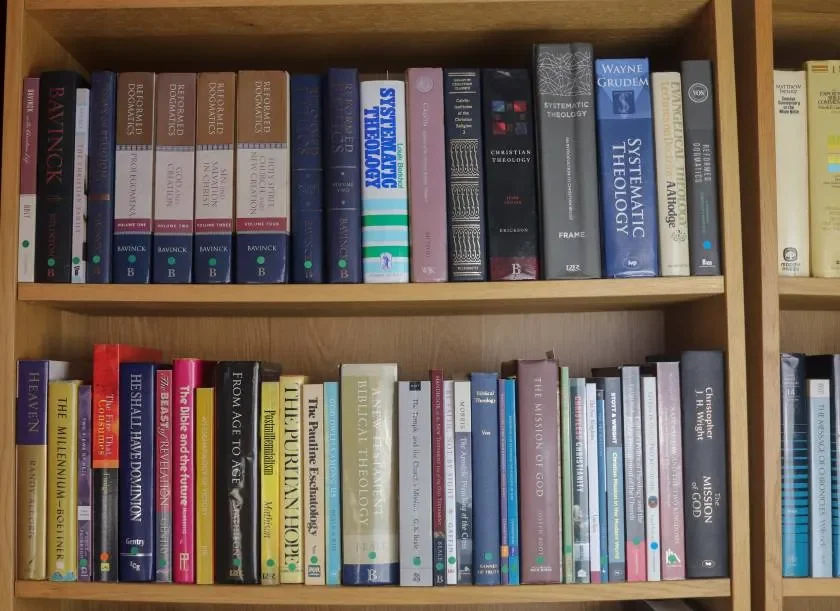 Bookshelf containing theology, philosophy, and religious books arranged on two wooden shelves.