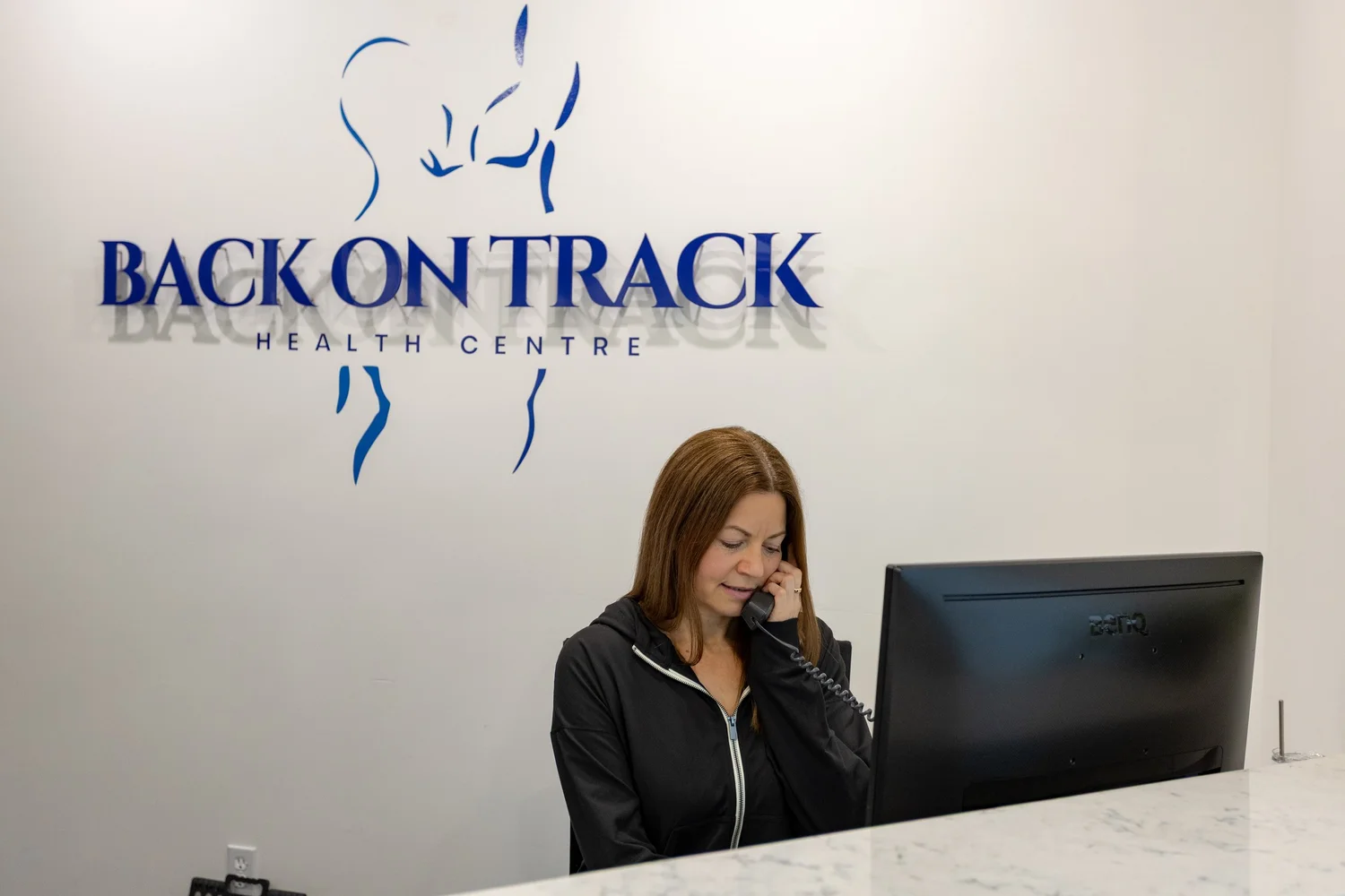 Back On Track Health Centre receptionist assisting a caller at the Spruce Grove front desk