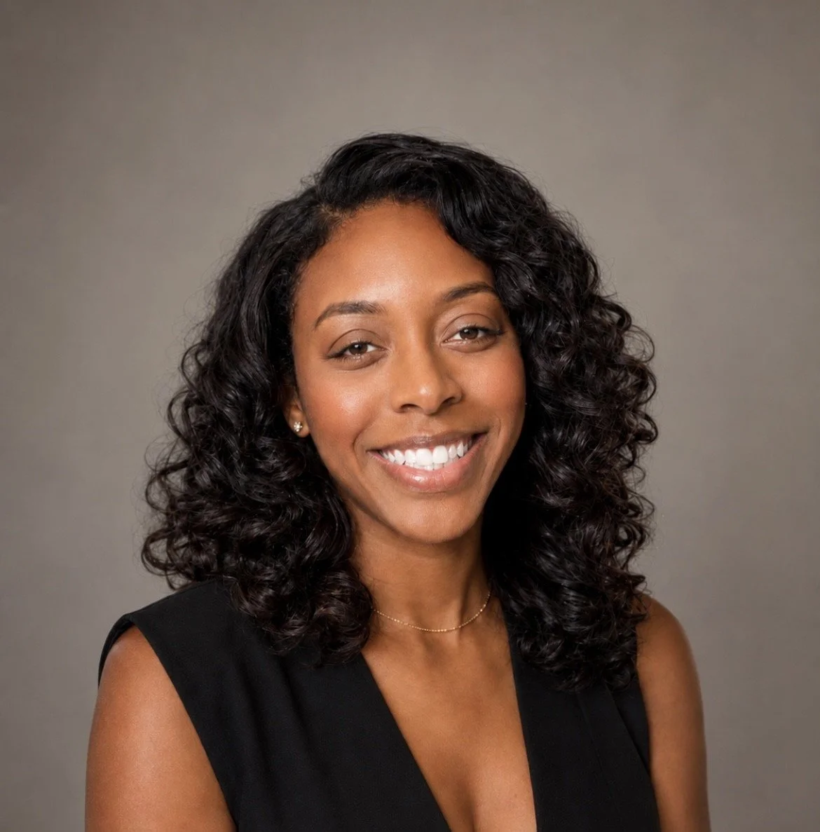 Portrait of a smiling Black woman with curly hair, wearing a black sleeveless top and small earrings, against a neutral background.
