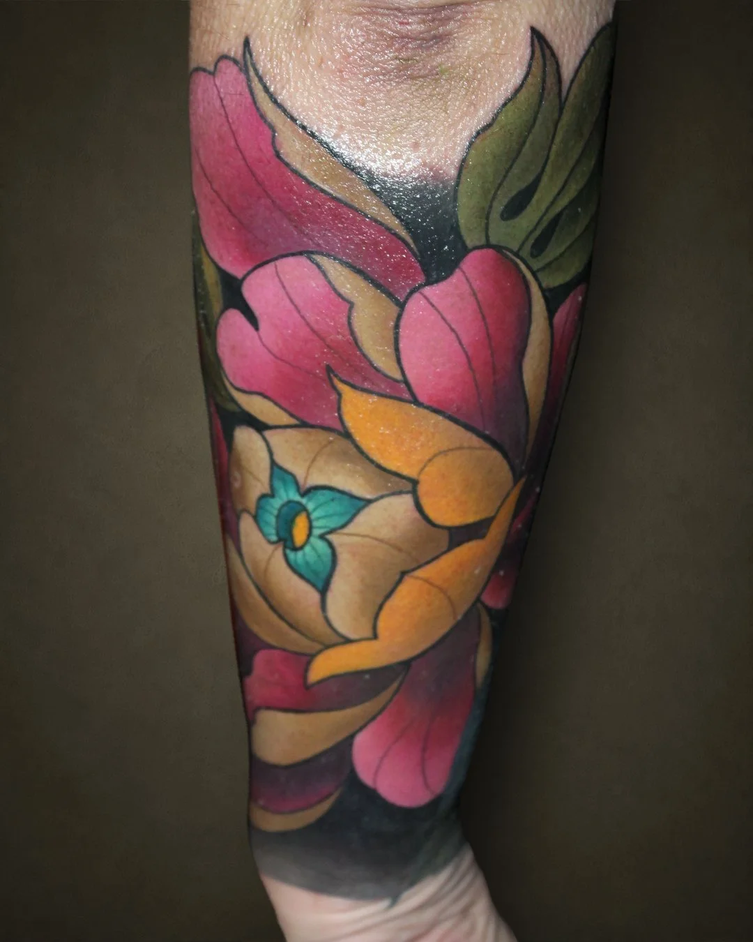 A colorful floral tattoo sleeve on a person's arm featuring pink, yellow, orange, and green flowers and leaves with black outlines.