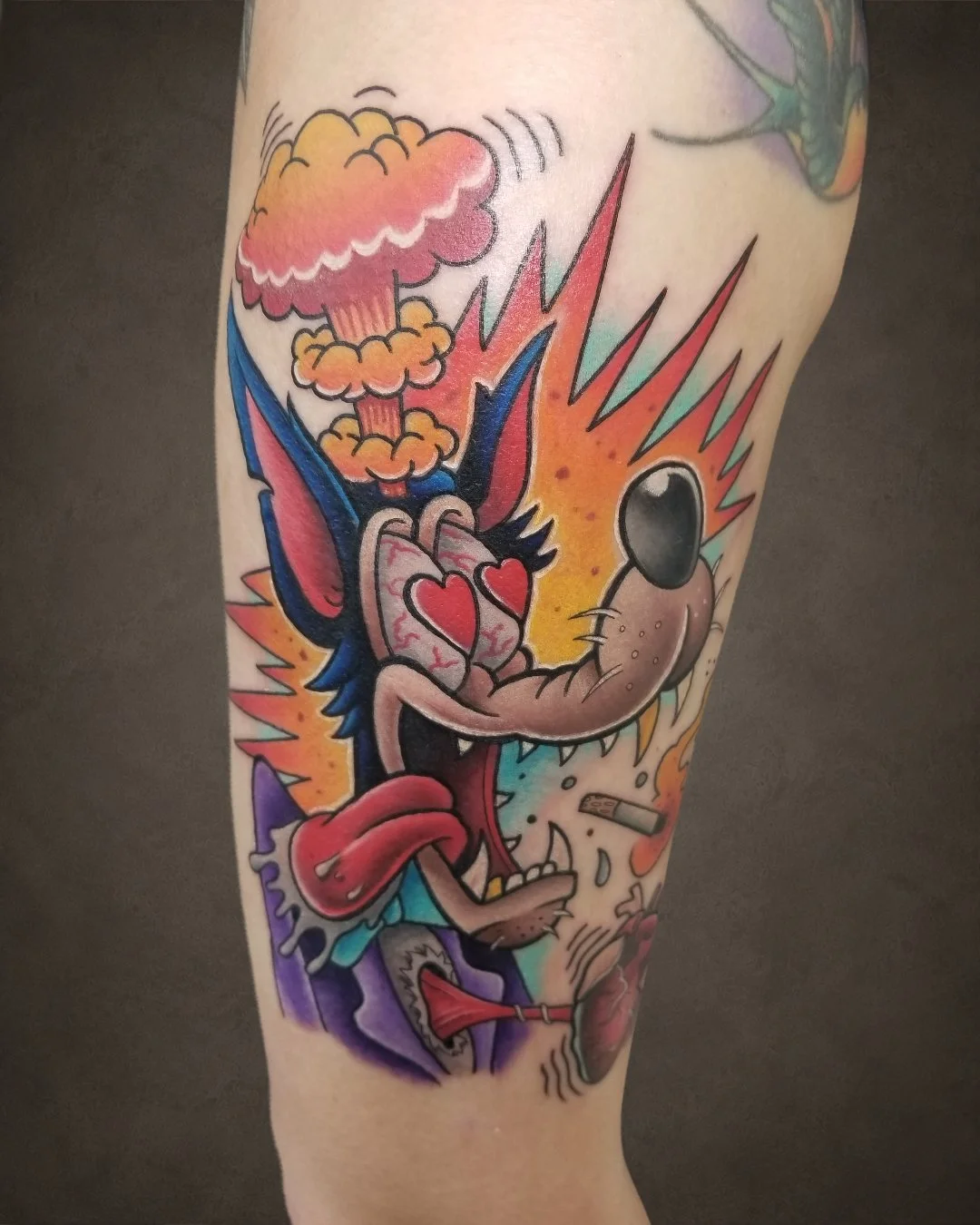 Colorful tattoo of a cartoon wolf with heart-shaped eyes and tongue out, surrounded by explosions and vibrant colors.