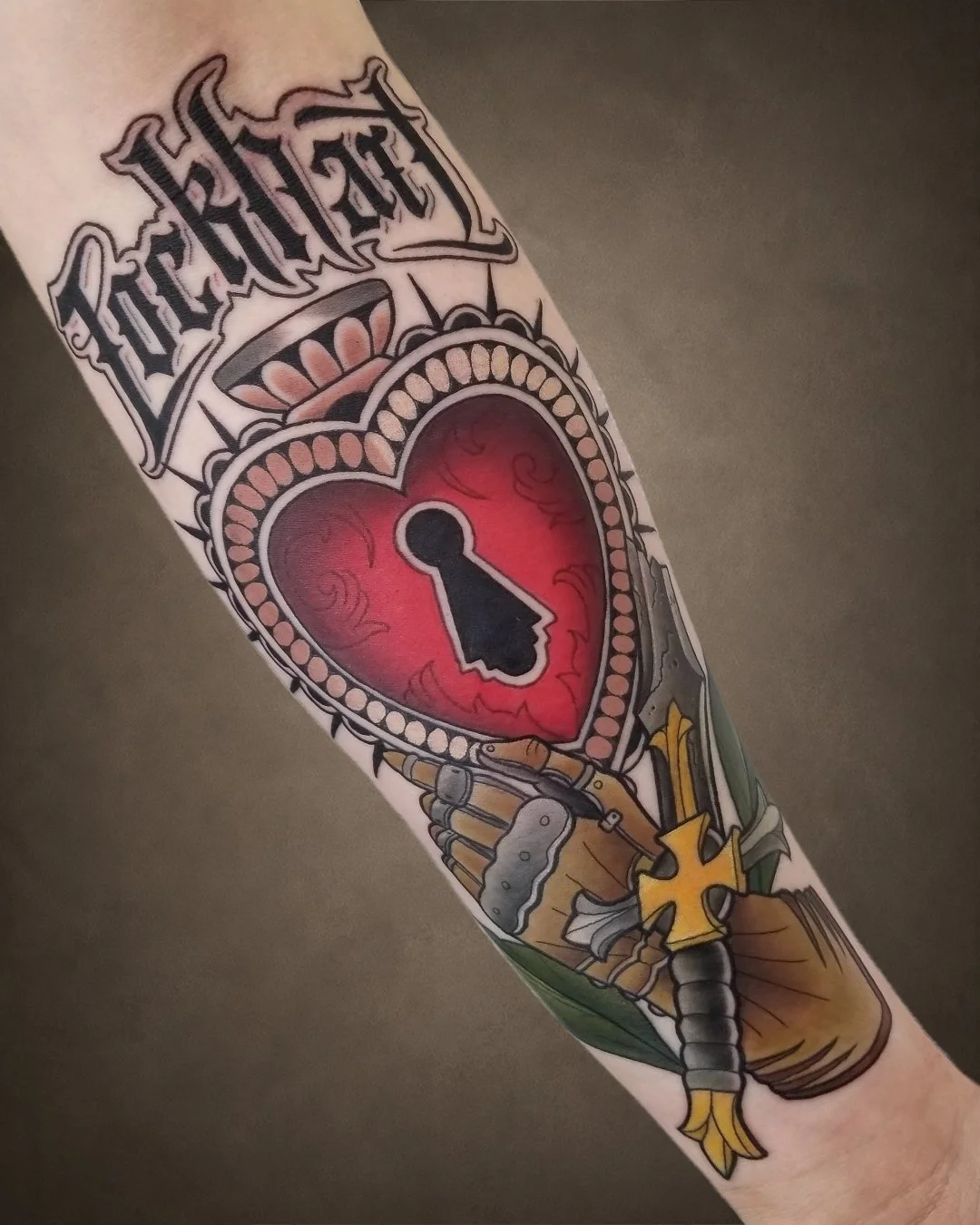 Tattoo of a heart with a keyhole, surrounded by a dagger, a cross, and the word "Faith" in old English font.