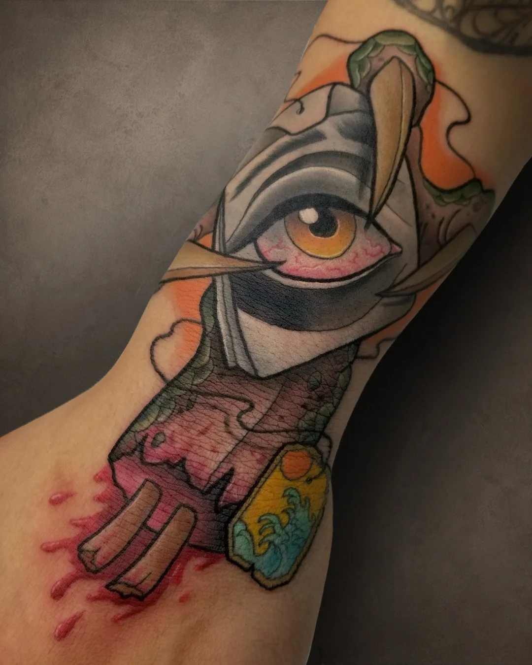 Tattoo of a stylized eye with vibrant colors, surrounded by abstract and traditional tattoo elements, on a person's arm.