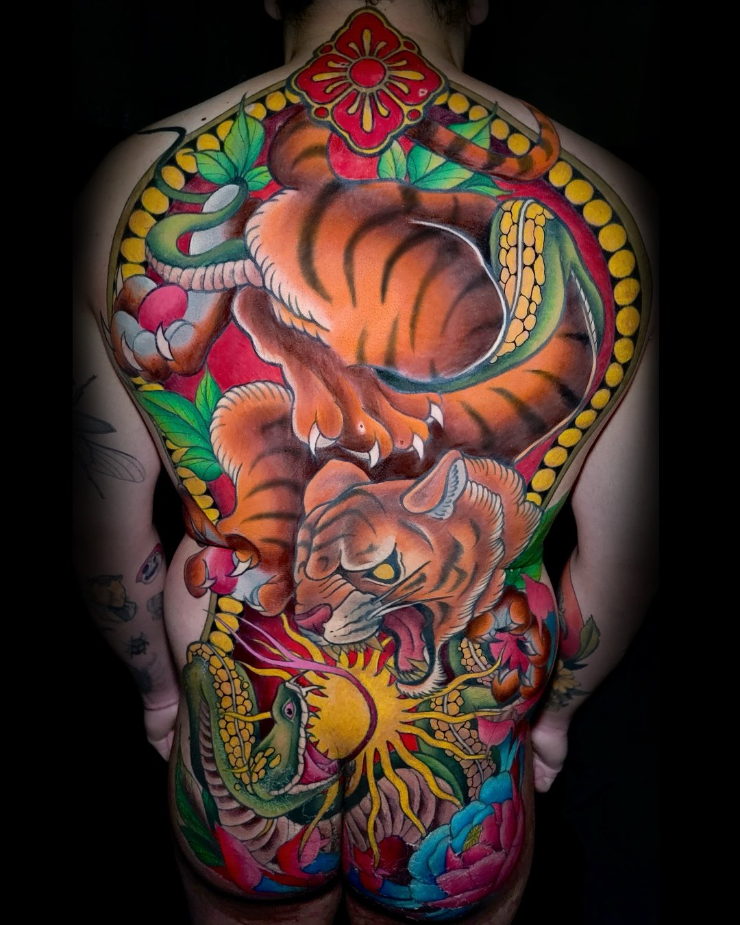 Vibrant Neo-Traditional full back tattoo featuring a tiger and snake intertwined with bold ornamental elements.