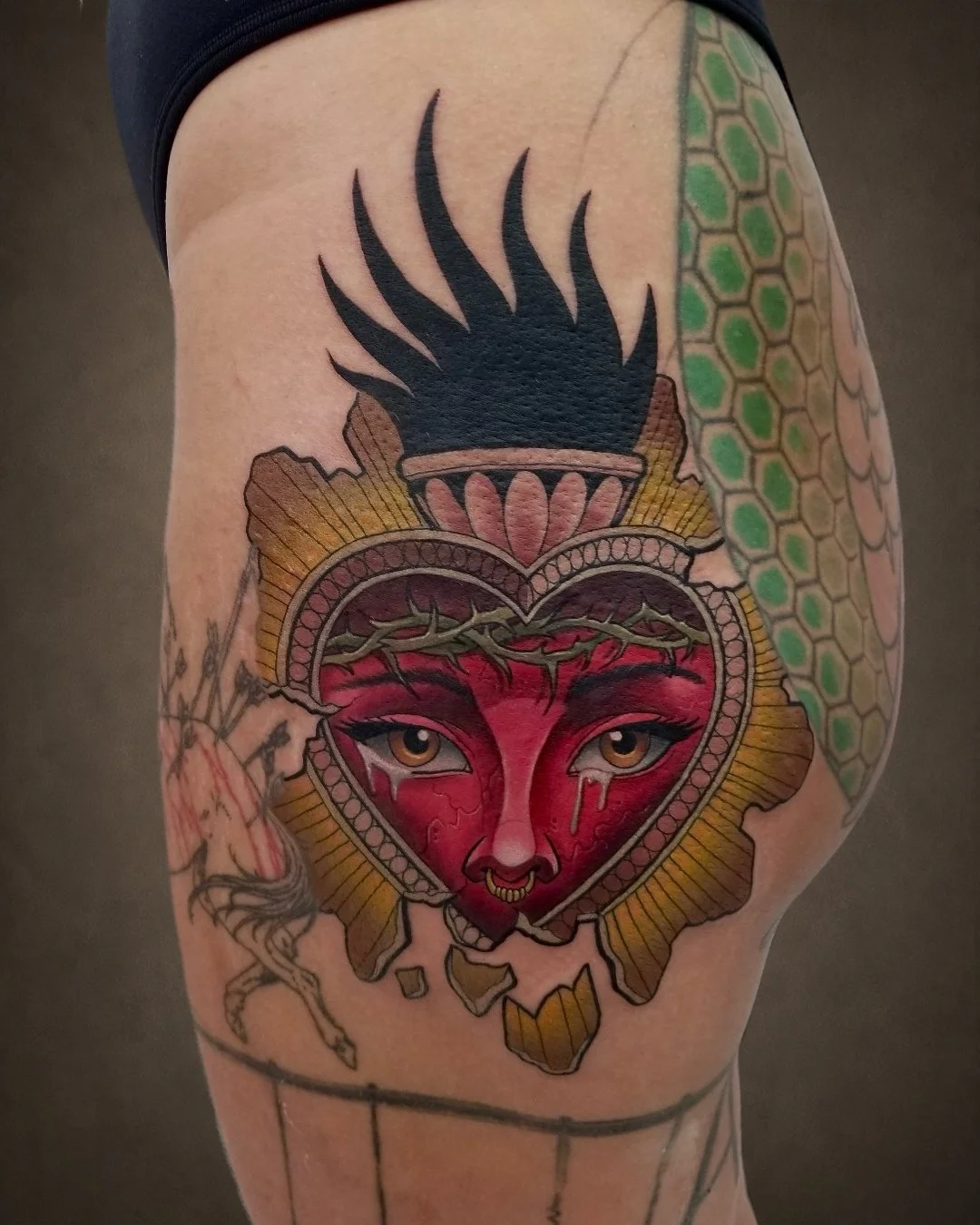 Tattoo of a red heart with a woman's face, with detailed eyes and lips, surrounded by ornate patterns and a black flame-like design above.