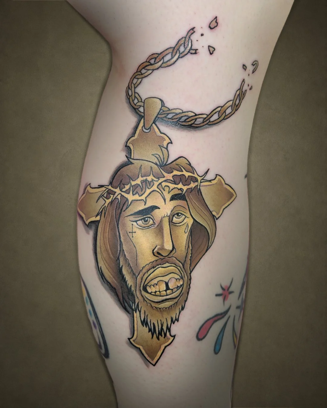 Tattoo of Jesus Christ with a crown of thorns and a tear drop, wearing a chain around his neck, on a person's arm.