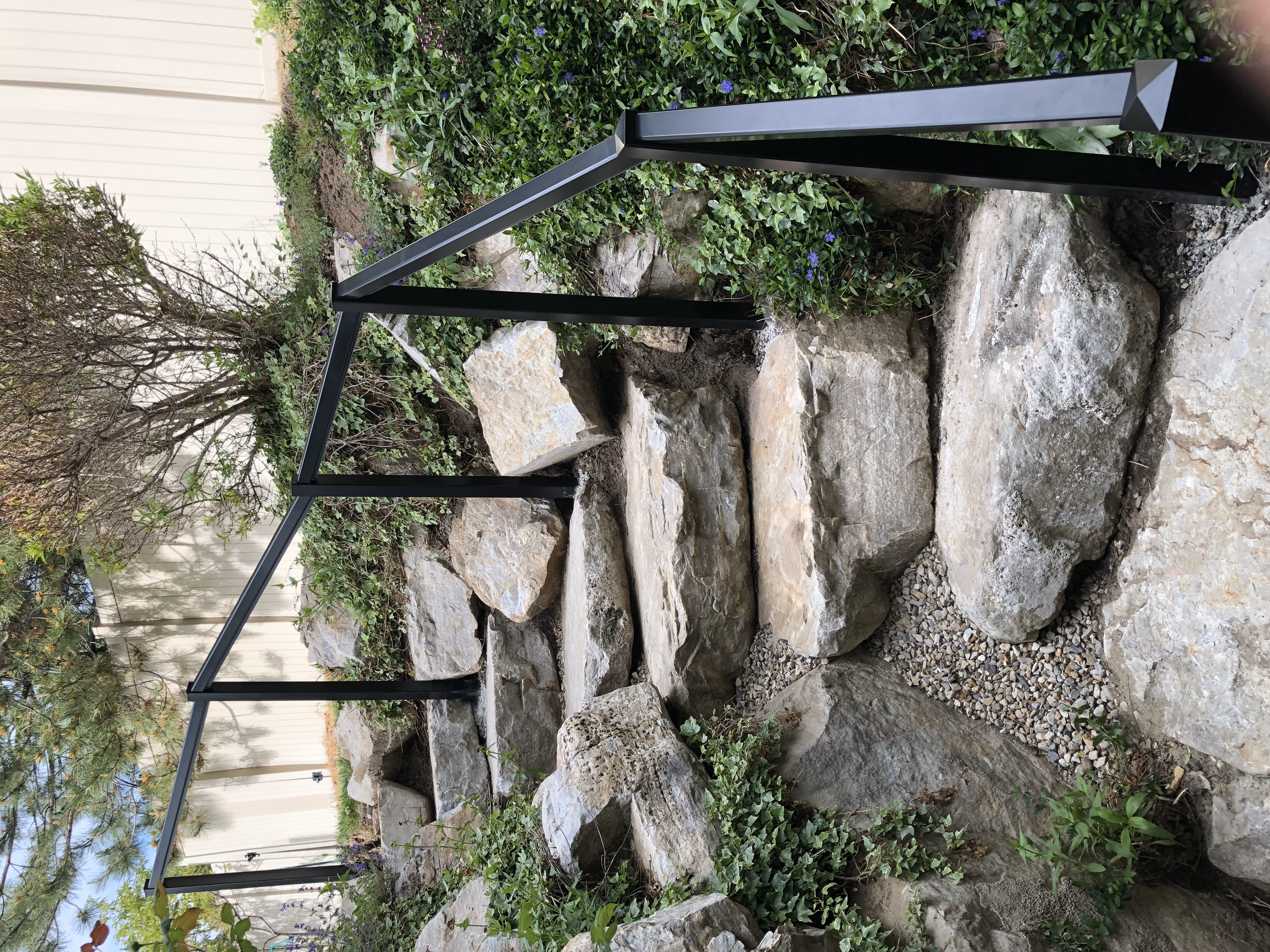 Stone staircase with metal handrail outdoors, surrounded by greenery and a white fence.