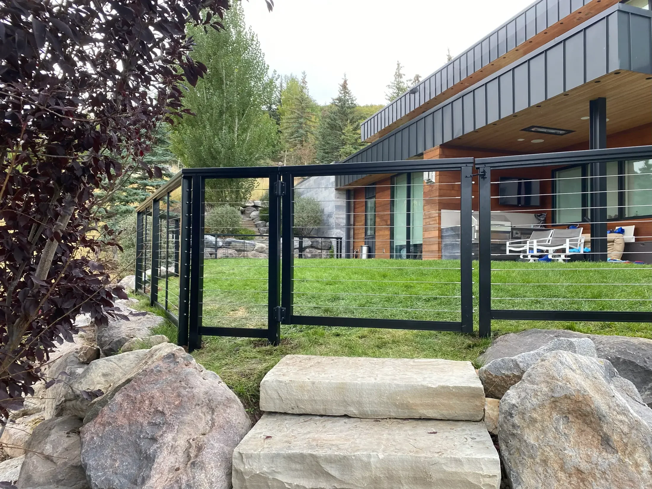 Step stones leading onto a yard with a modern house, surrounded by rocks and greenery.