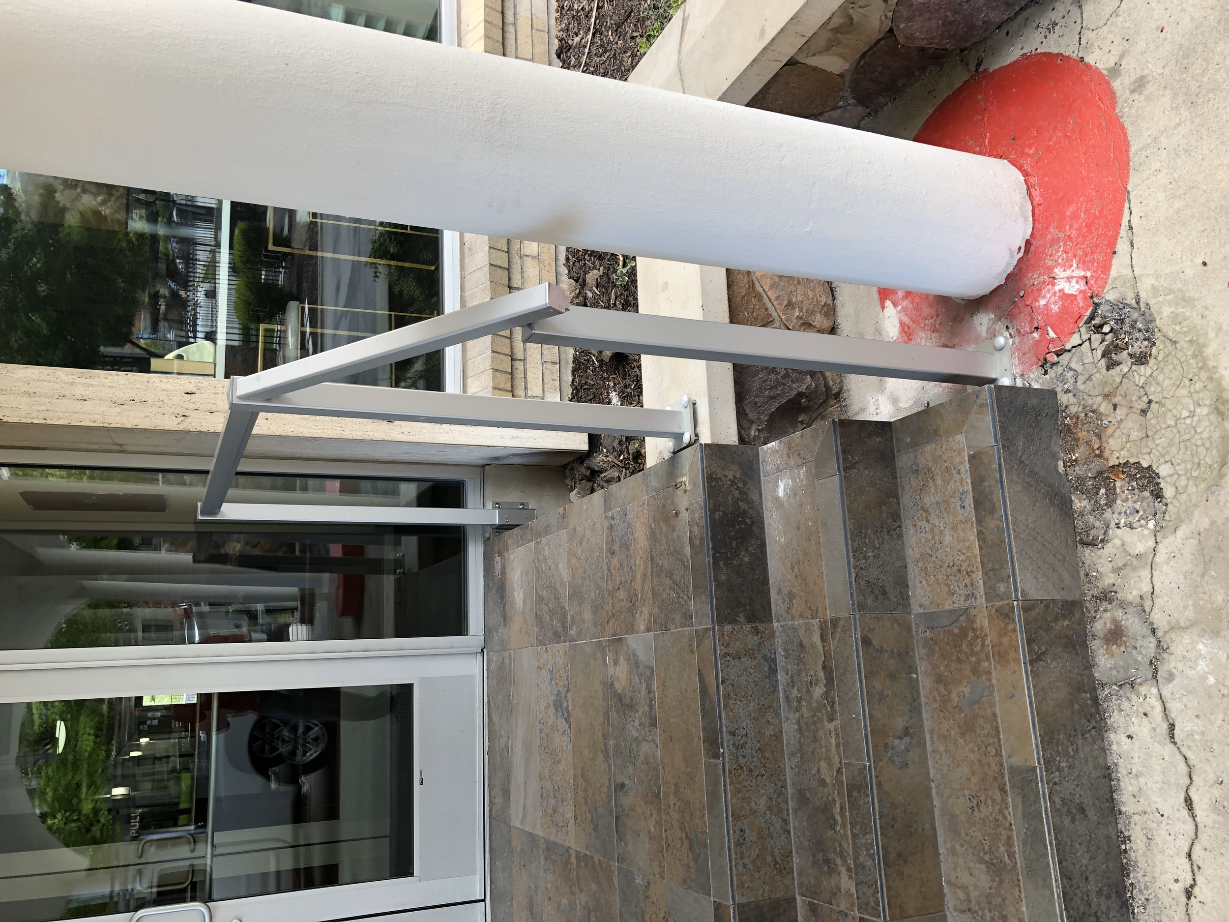 Construction site at building entrance with steps, handrail, damaged concrete, and a column with white paint and red patch.