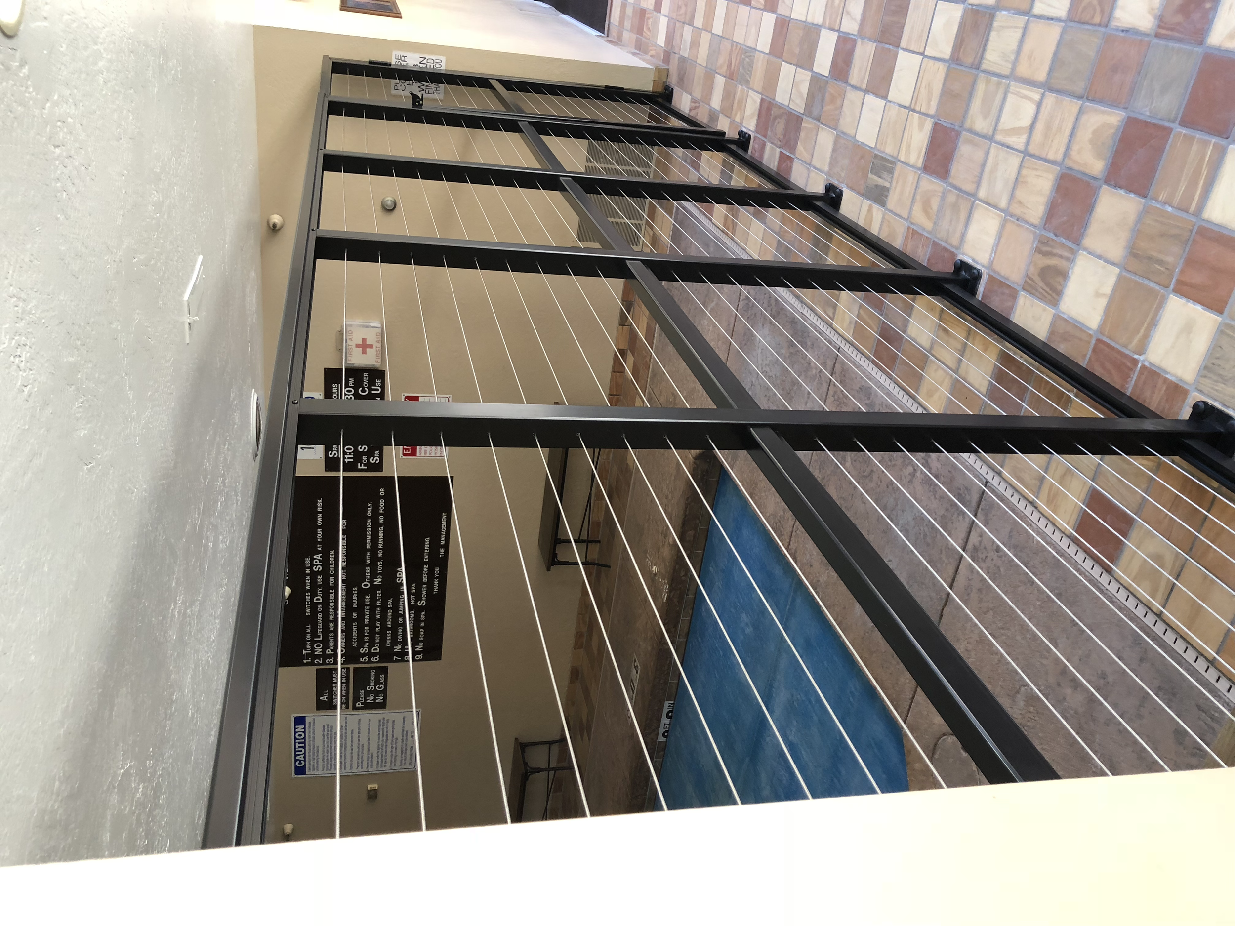 Entrance to a spa with a safety railing and signage on the wall, including emergency and safety instructions, in a tiled corridor.